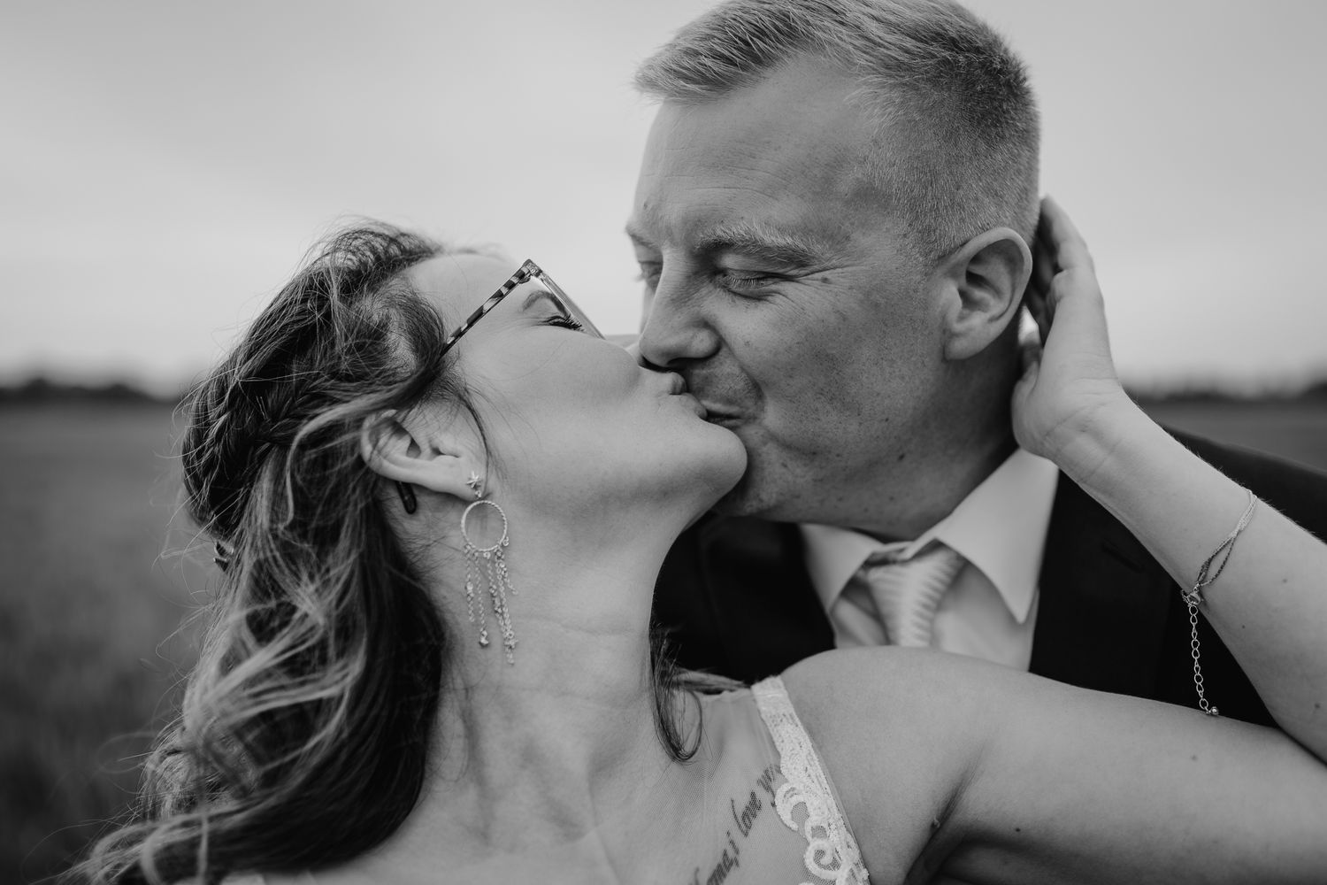A romantic black and white wedding photograph of a couple sharing an intimate kiss in a countryside setting.