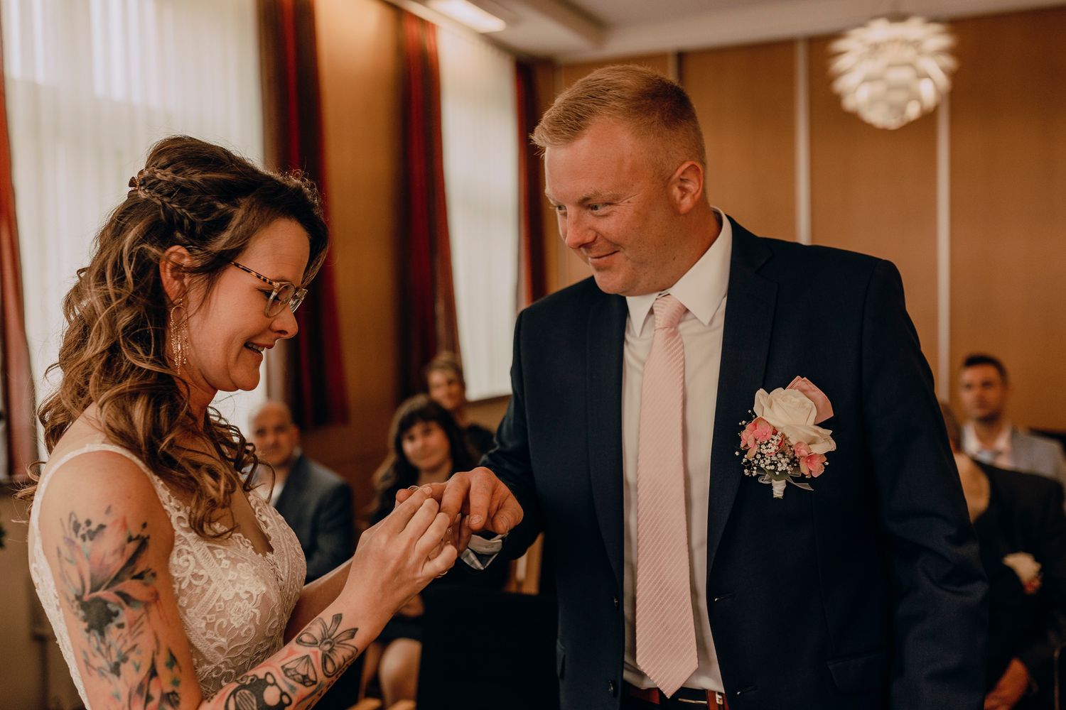 An emotional moment between two people during a wedding ceremony, with pink floral boutonniere and elegant attire.