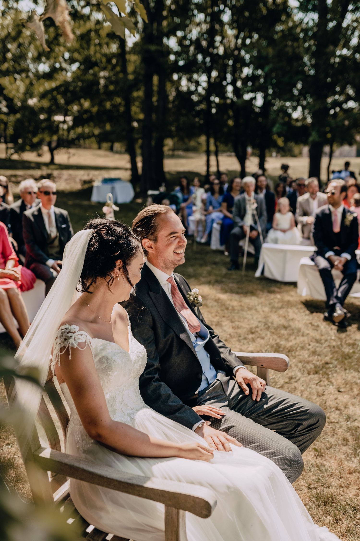 Outdoor wedding ceremony seating arrangement with guests watching couple during summer celebration.