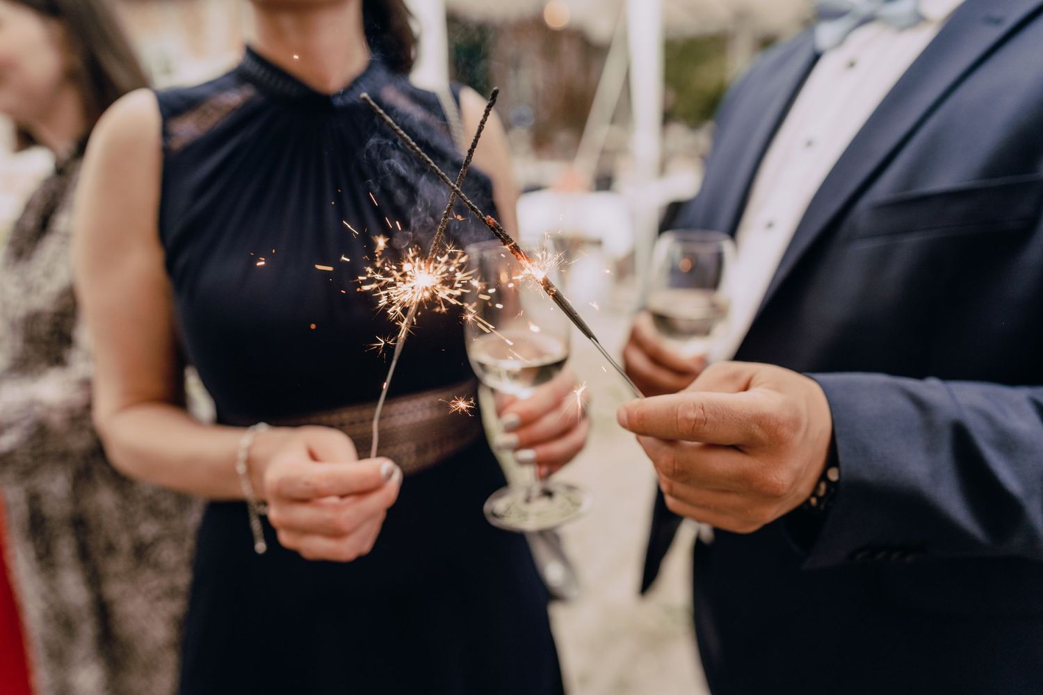 Wedding guests hold sparklers and champagne glasses during celebration.