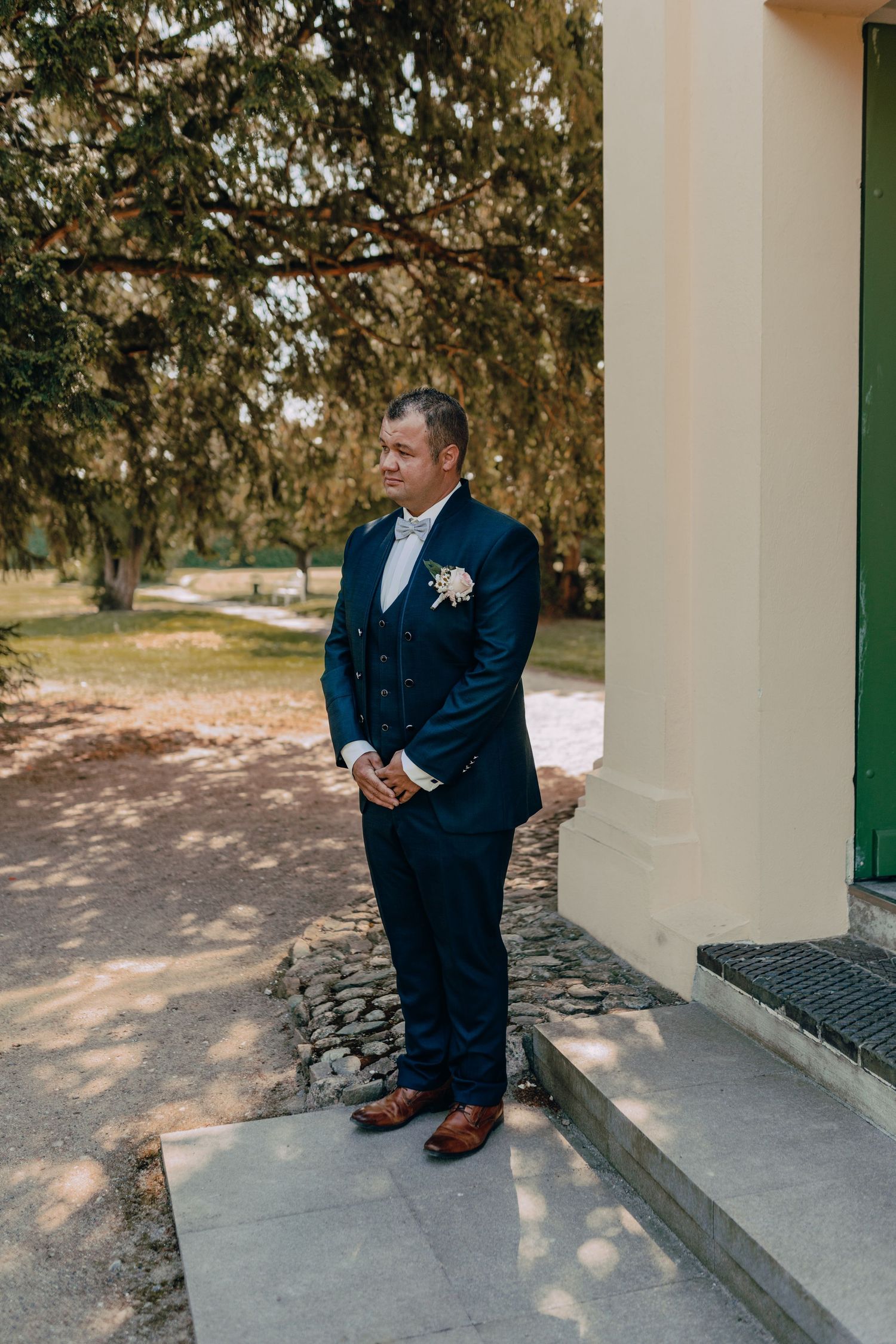 Sequence of shots showing groom checking phone while sitting on white porch steps in navy suit and brown shoes.