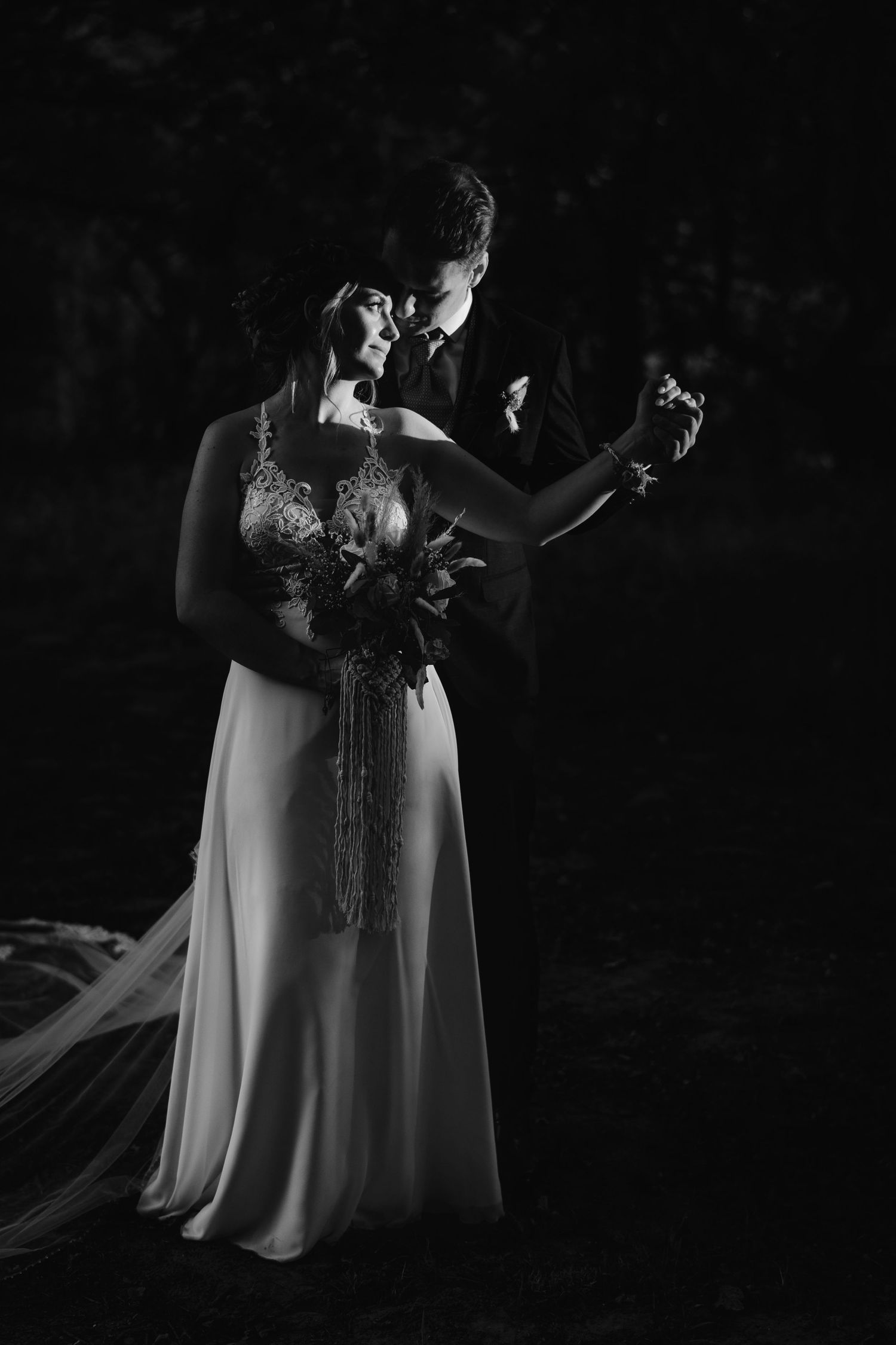 Dramatic black and white wedding photo of couple dancing together in elegant dress and formal attire.