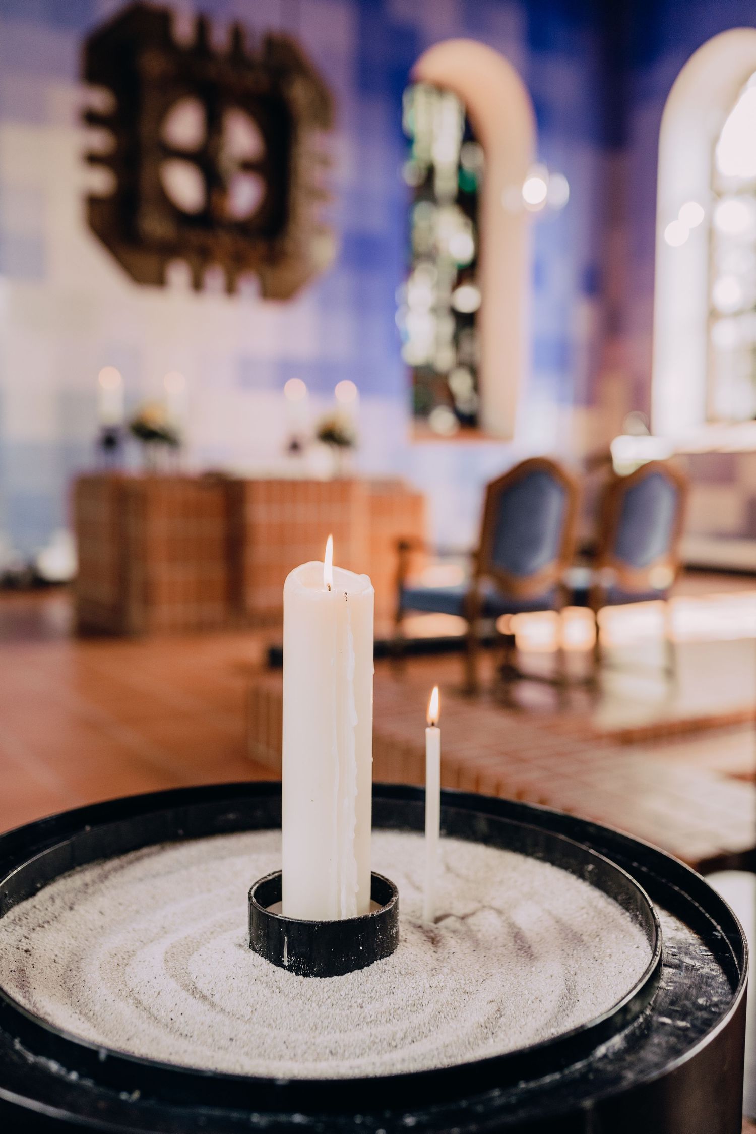 Four connected photos show a white candle on a dark circular base with decorative sand or grain patterns in a church setting.