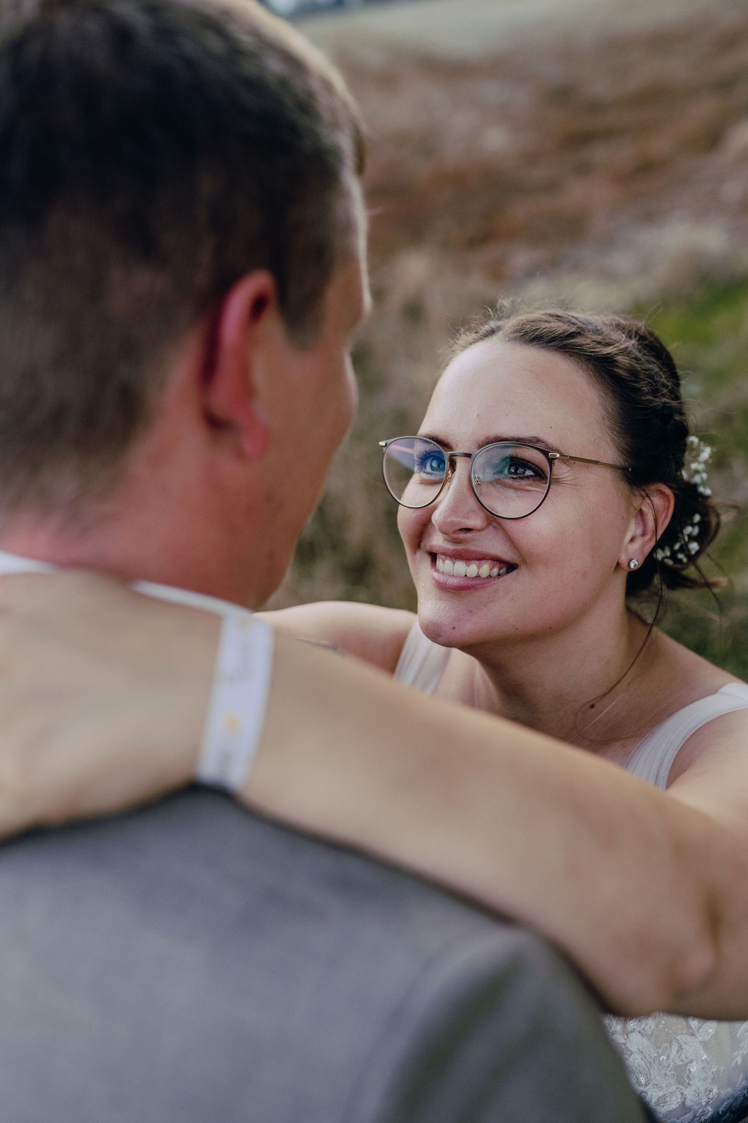 Couple in love share an intimate moment during outdoor photo session, bride wearing glasses smiles warmly.