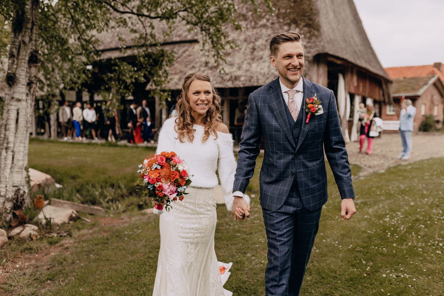Wedding couple walking outdoors on grassy grounds of a rustic venue.