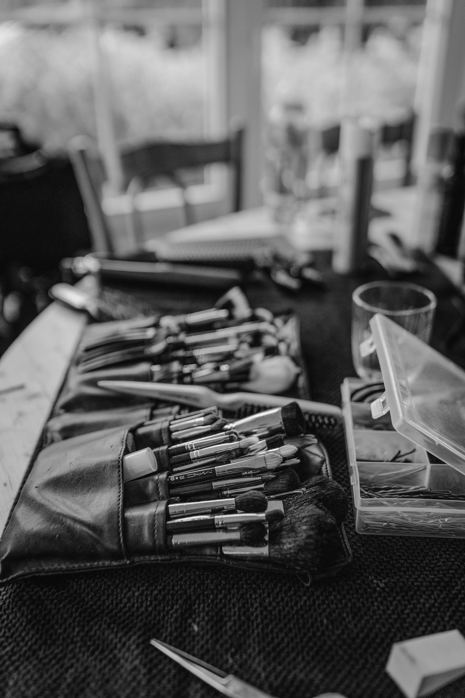 Professional makeup brushes arranged in a row on black textured surface in dramatic monochrome lighting.