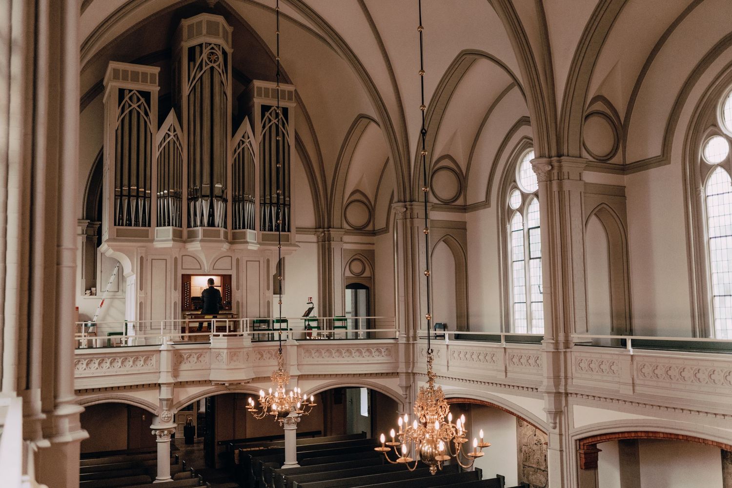 Interior of a grand church with vaulted arches, chandeliers, and a pipe organ at the altar.