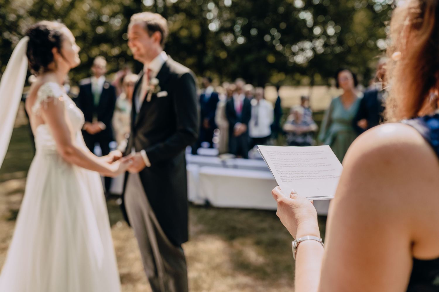 Outdoor wedding ceremony with couple exchanging vows under trees.
