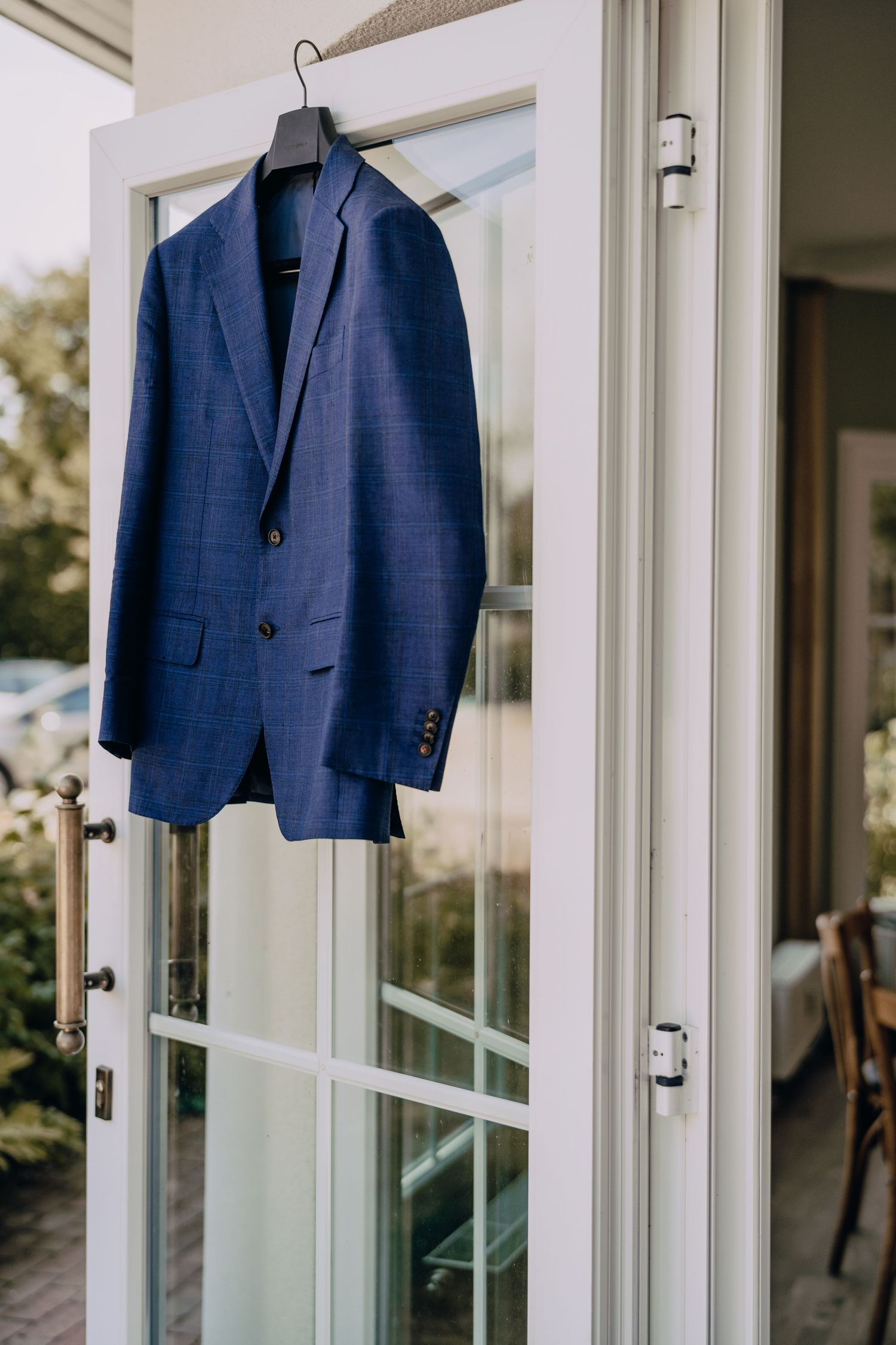 Navy blue suit jackets hanging on white wooden french doors in preparation for a formal event.