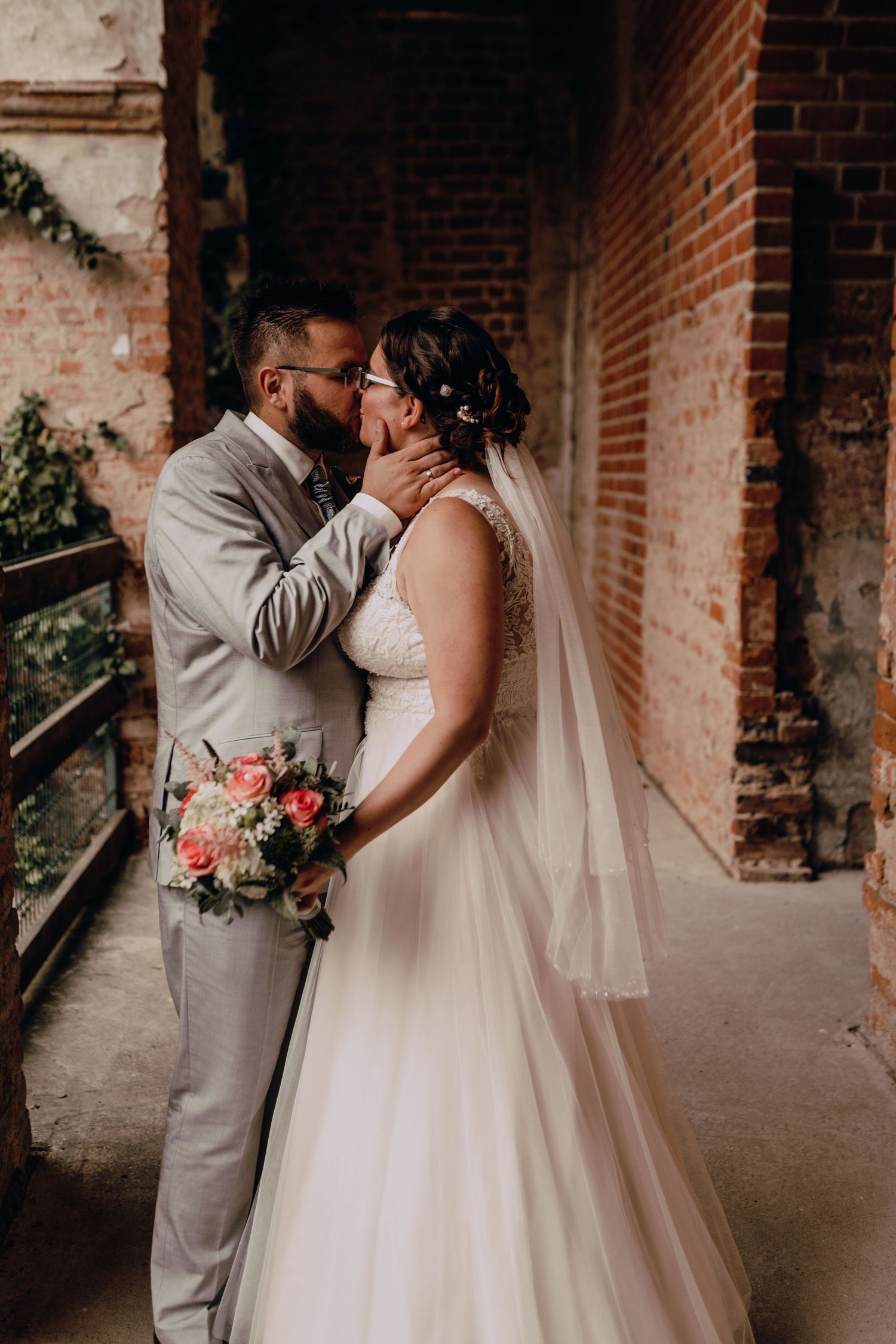 A romantic wedding moment captured against rustic brick walls with pink floral bouquet.