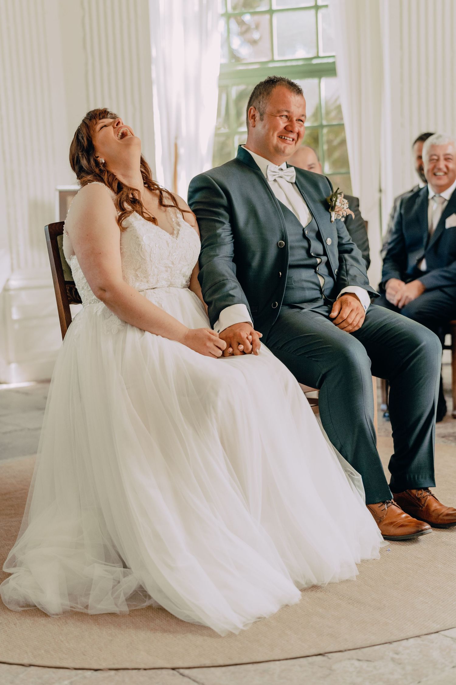 A candid moment of laughter during a wedding ceremony shows joy between a couple in formal attire.