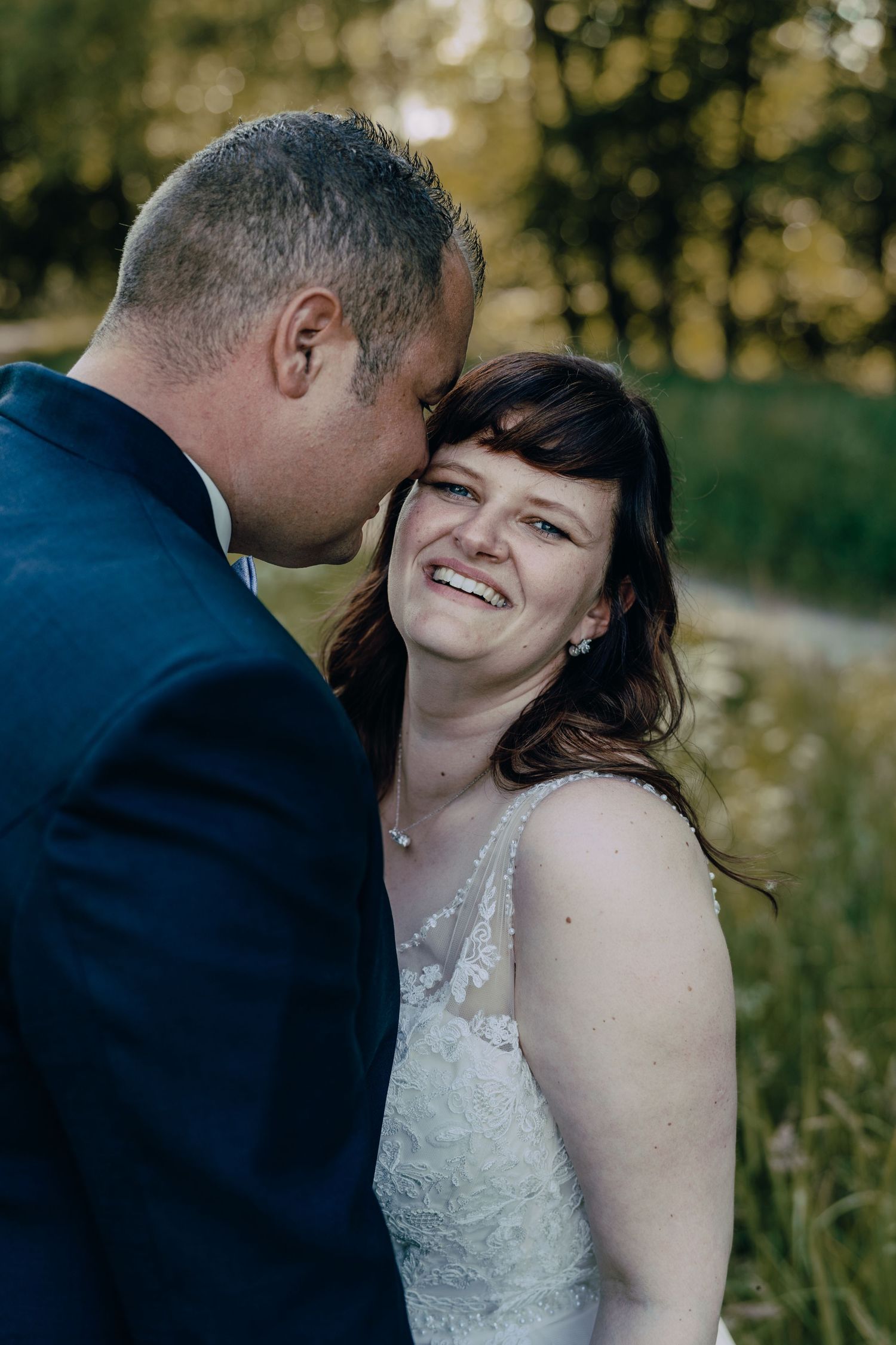 Wedding couple shares intimate moments and laughter against a sunlit natural outdoor backdrop.