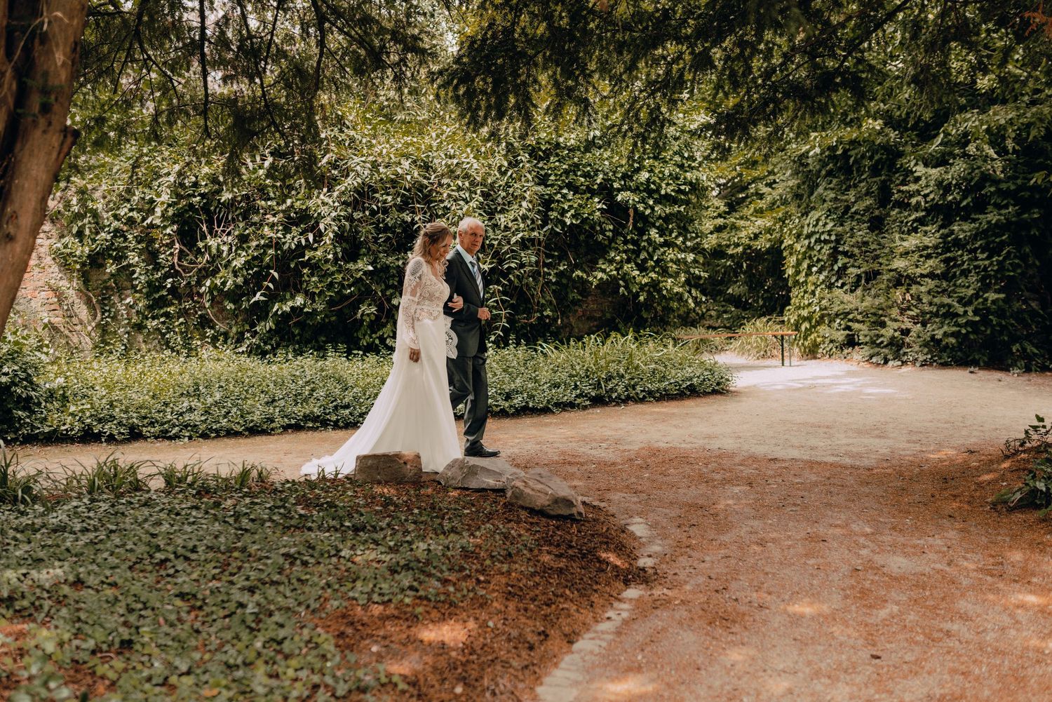 A newlywed couple shares an intimate moment on a winding garden path surrounded by lush greenery.