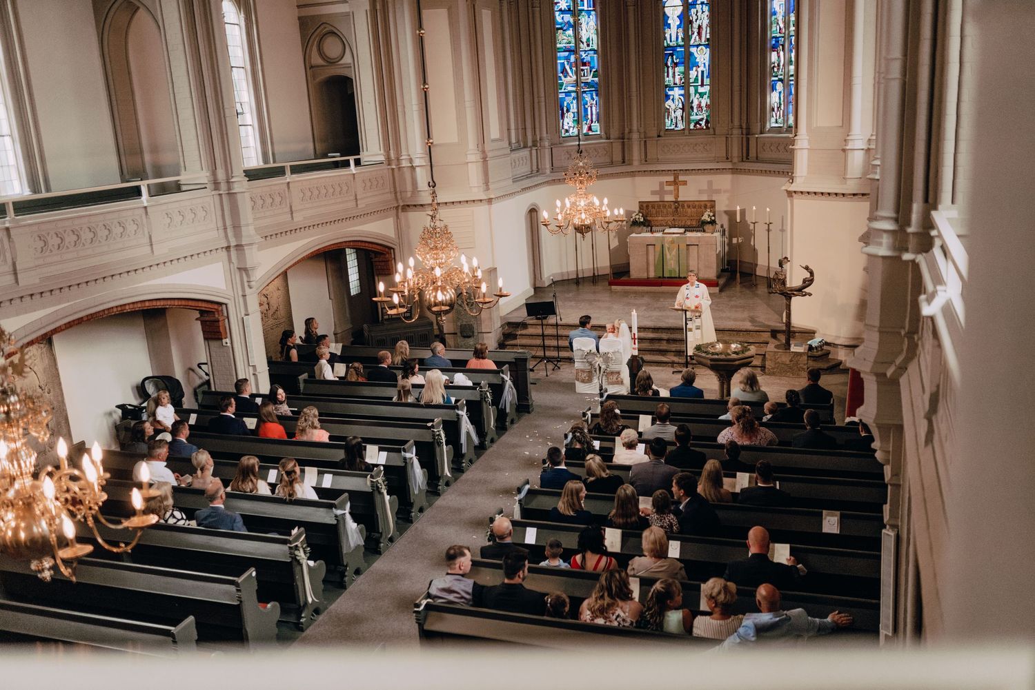 An elegant church interior filled with wooden pews and chandeliers during a wedding ceremony.