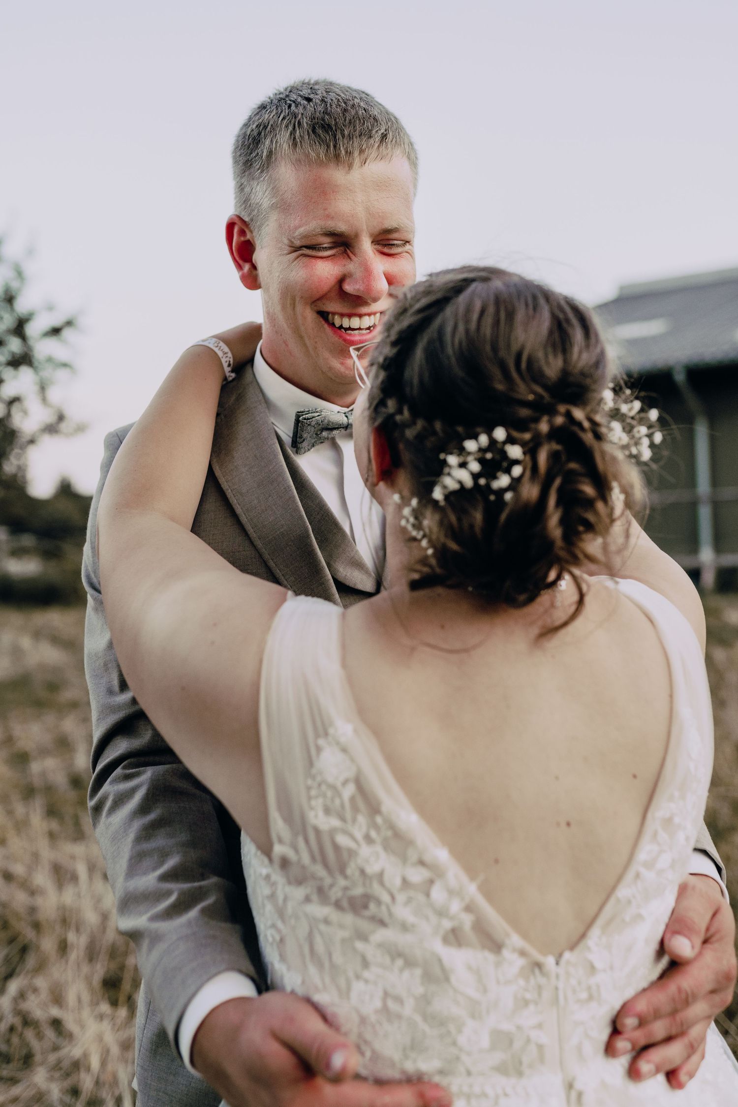 Couple shares joyful laughter and intimate embrace during outdoor wedding celebration with beautiful natural lighting.