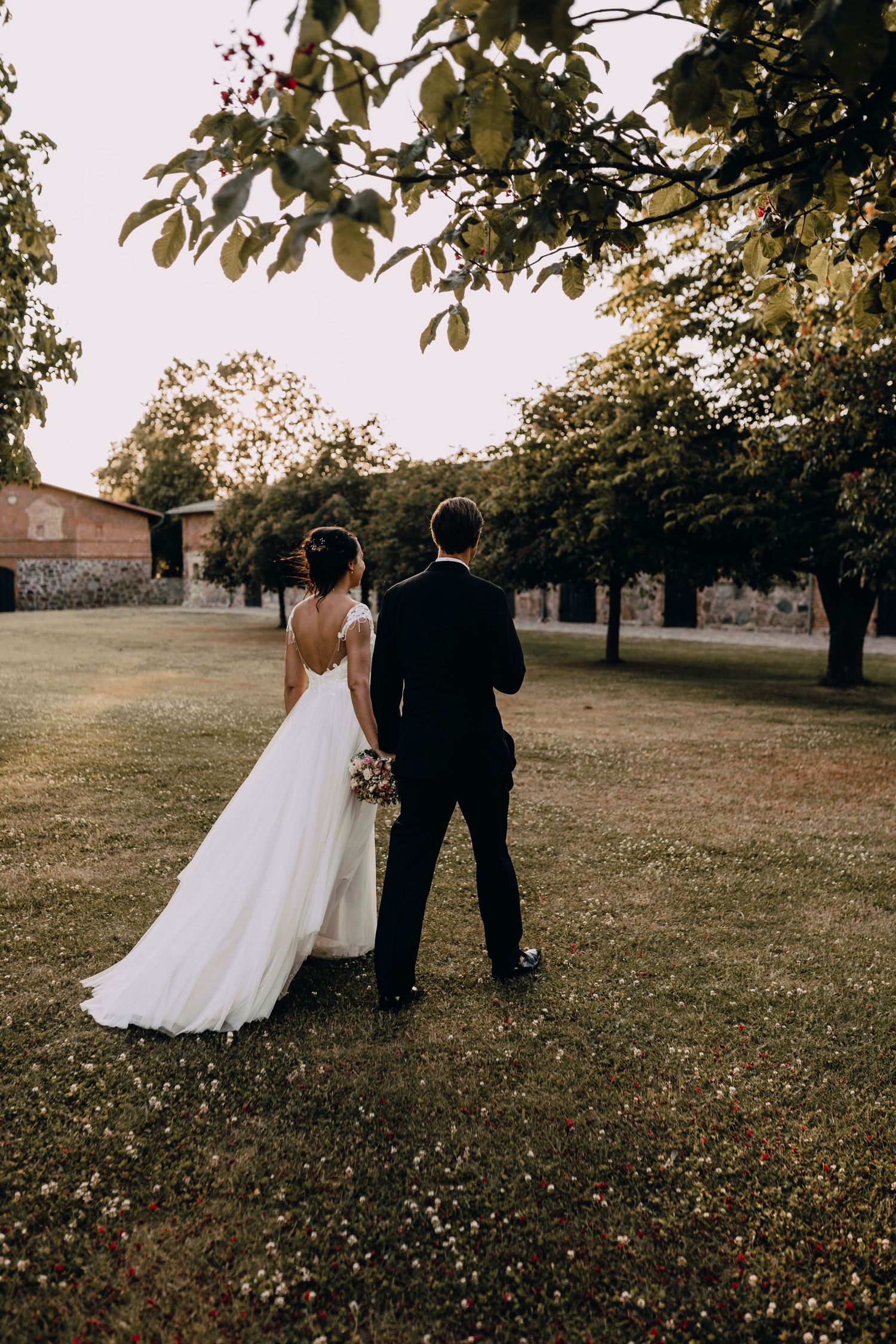 A newlywed couple shares an intimate moment while walking together on grassy grounds during golden hour light.