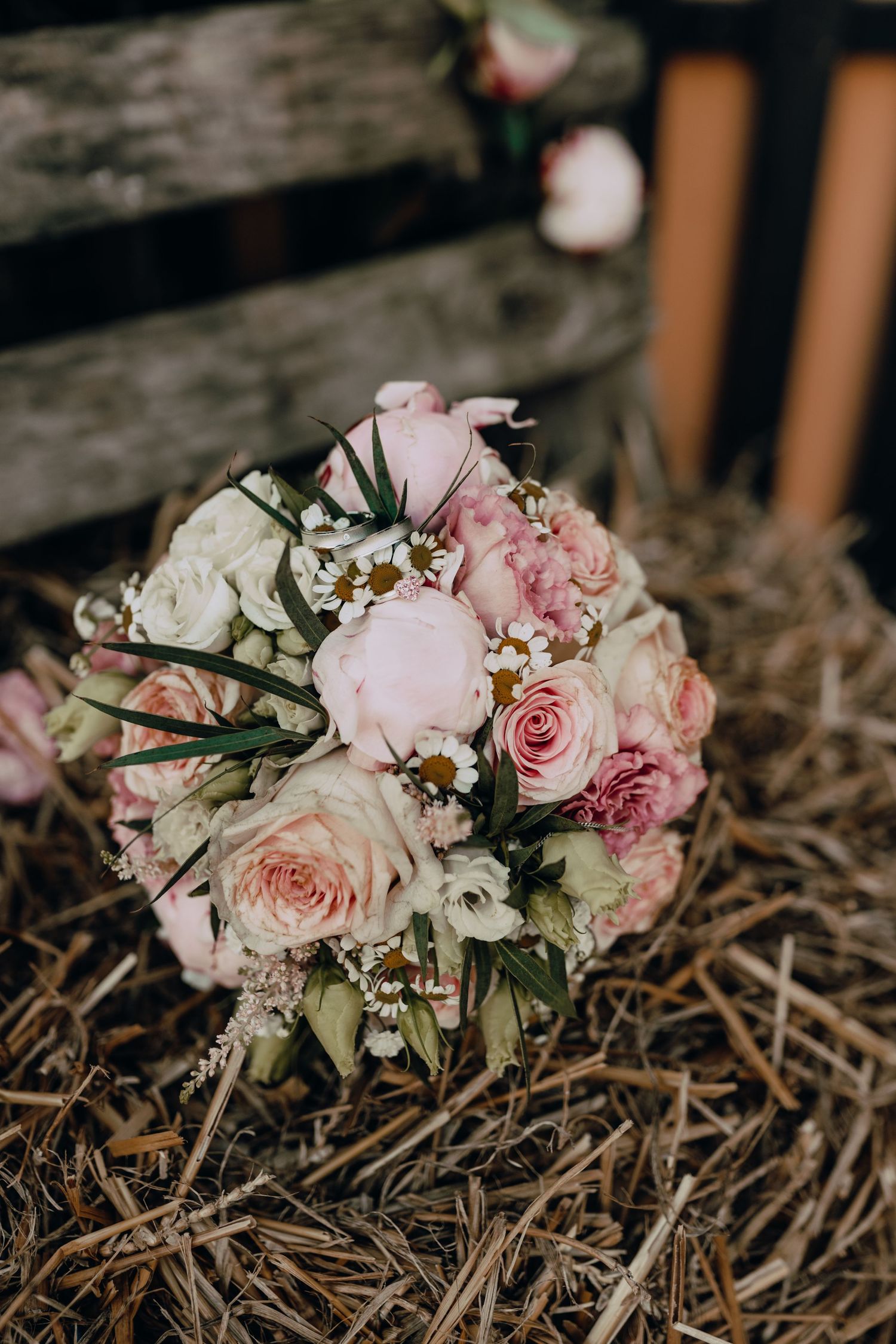 Beautiful bridal bouquet with soft pink roses and white flowers rests on rustic straw.