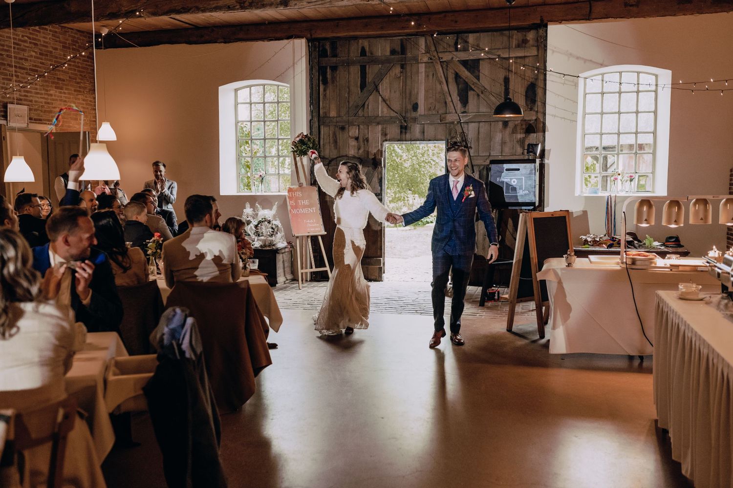 Newlyweds make their grand entrance into a rustic reception venue with exposed beams.