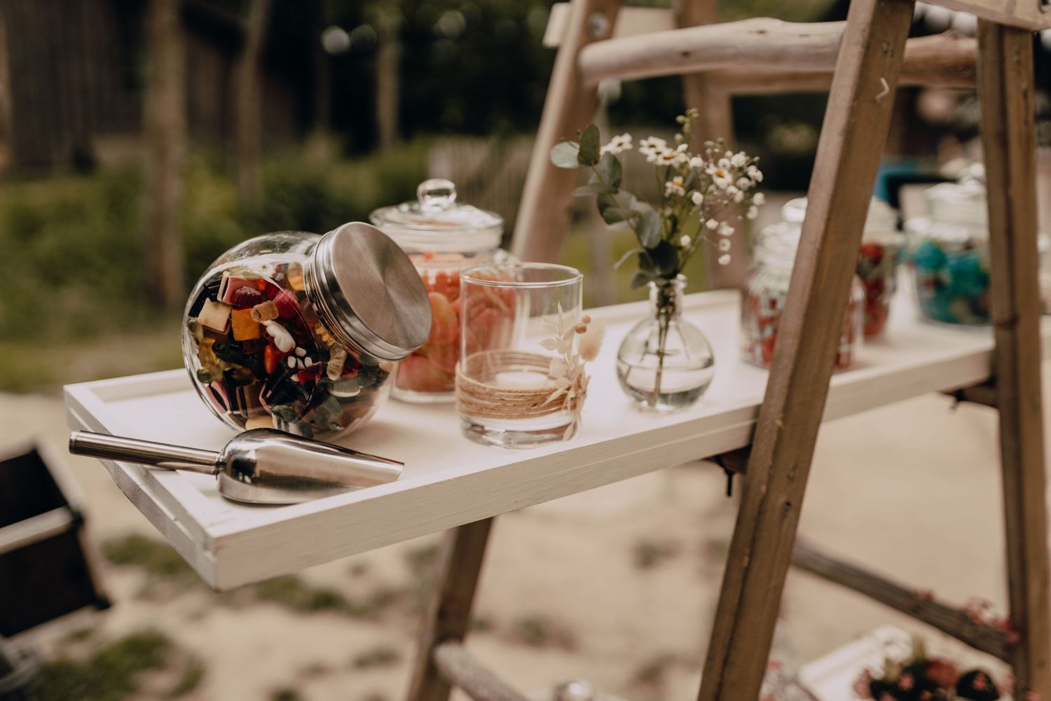 Rustic wedding reception setup featuring drinks and small vases on wooden ladder shelves.