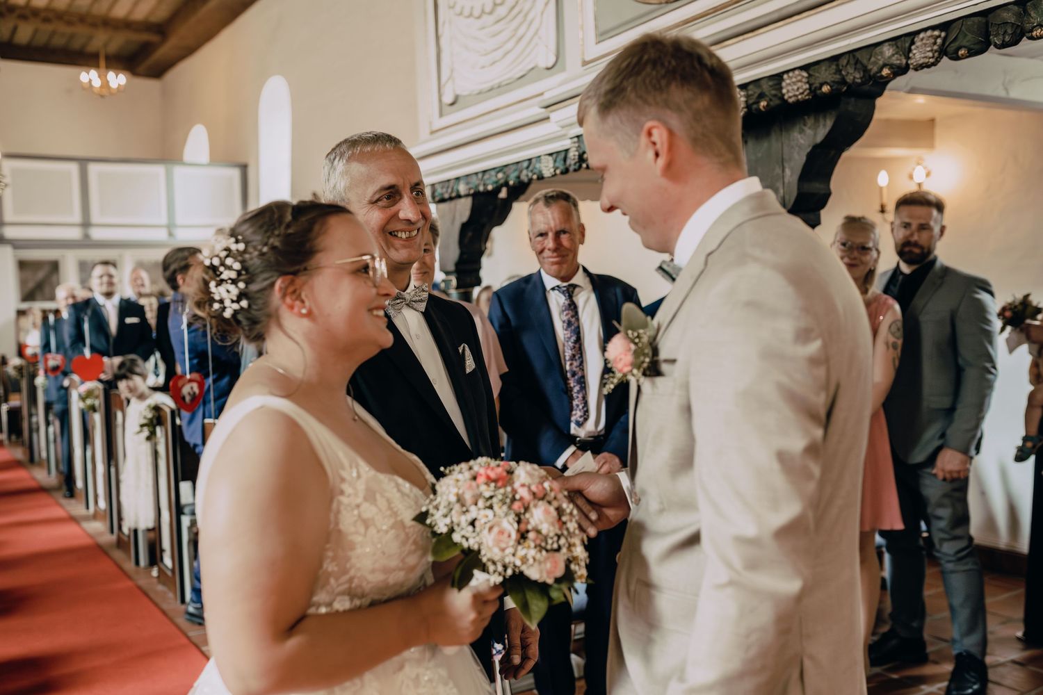 Wedding couple sharing romantic moments during ceremony while guests look on with joy in elegant indoor venue.