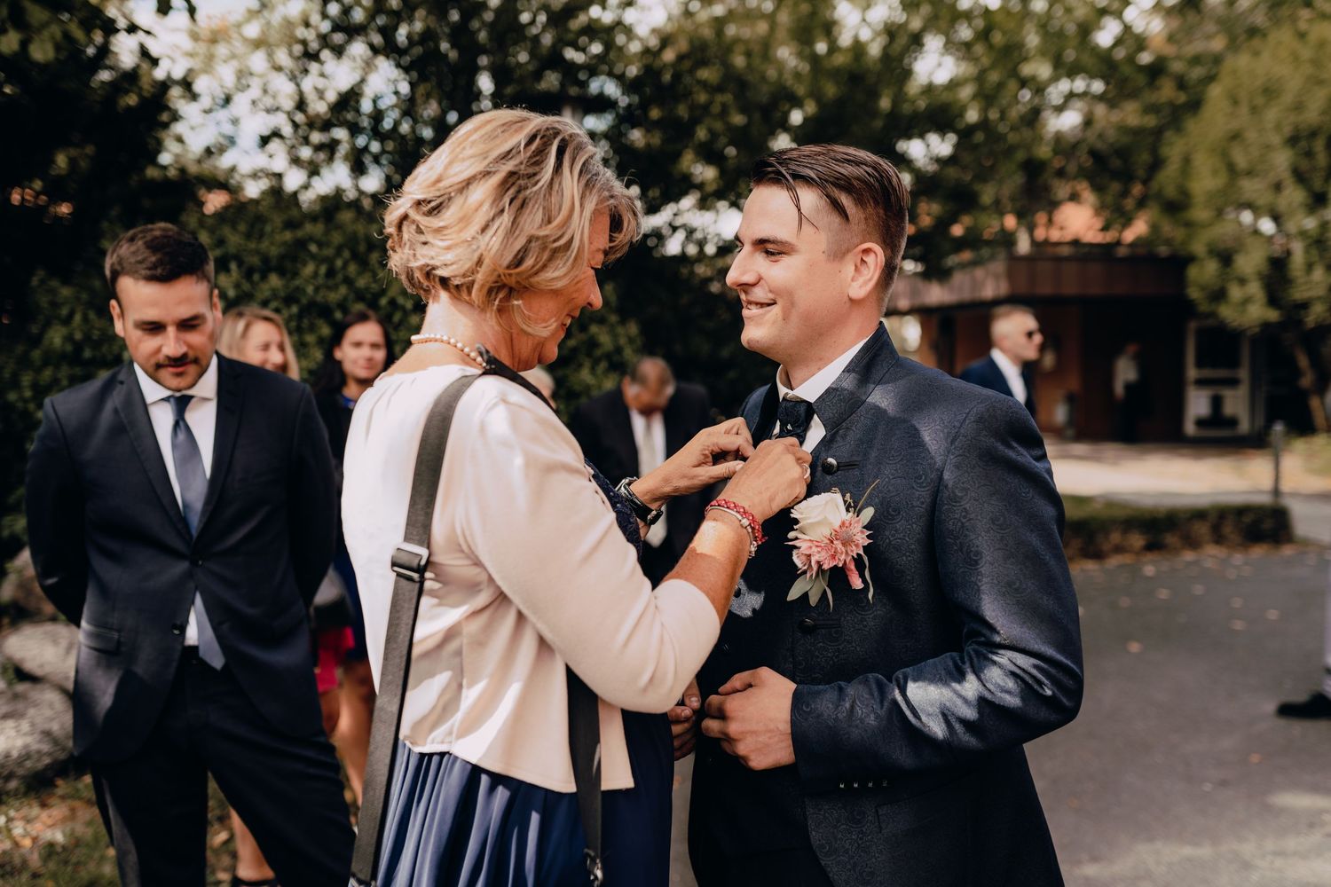 A guest wearing a white cardigan and navy skirt interacts with someone in a dark suit during an outdoor event.