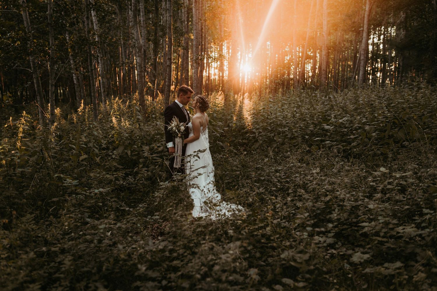 Person in white wedding dress standing in a sunlit forest during golden hour.
