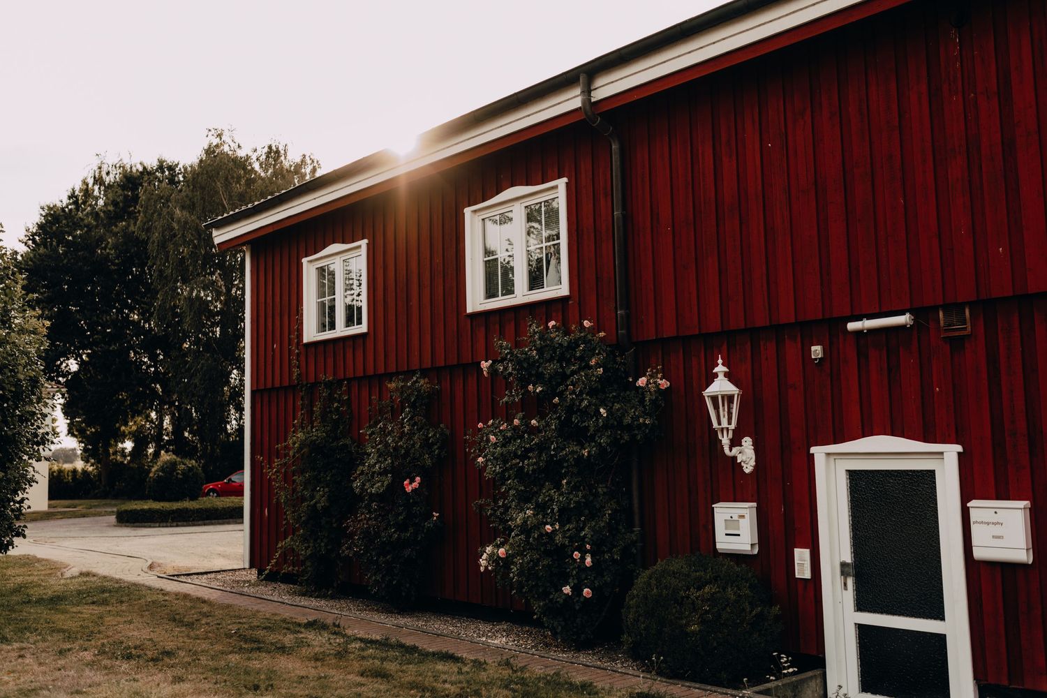 Red barn-style buildings with white trim set against a countryside landscape.