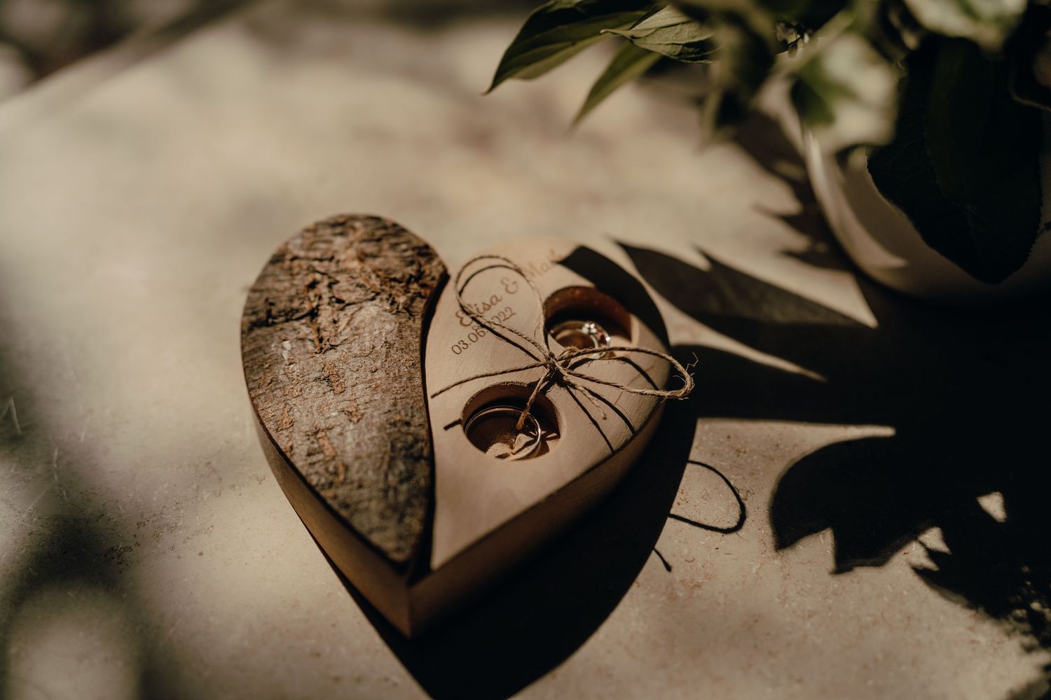 A wooden heart decoration with string tied around it casts shadows on a neutral surface in moody lighting.