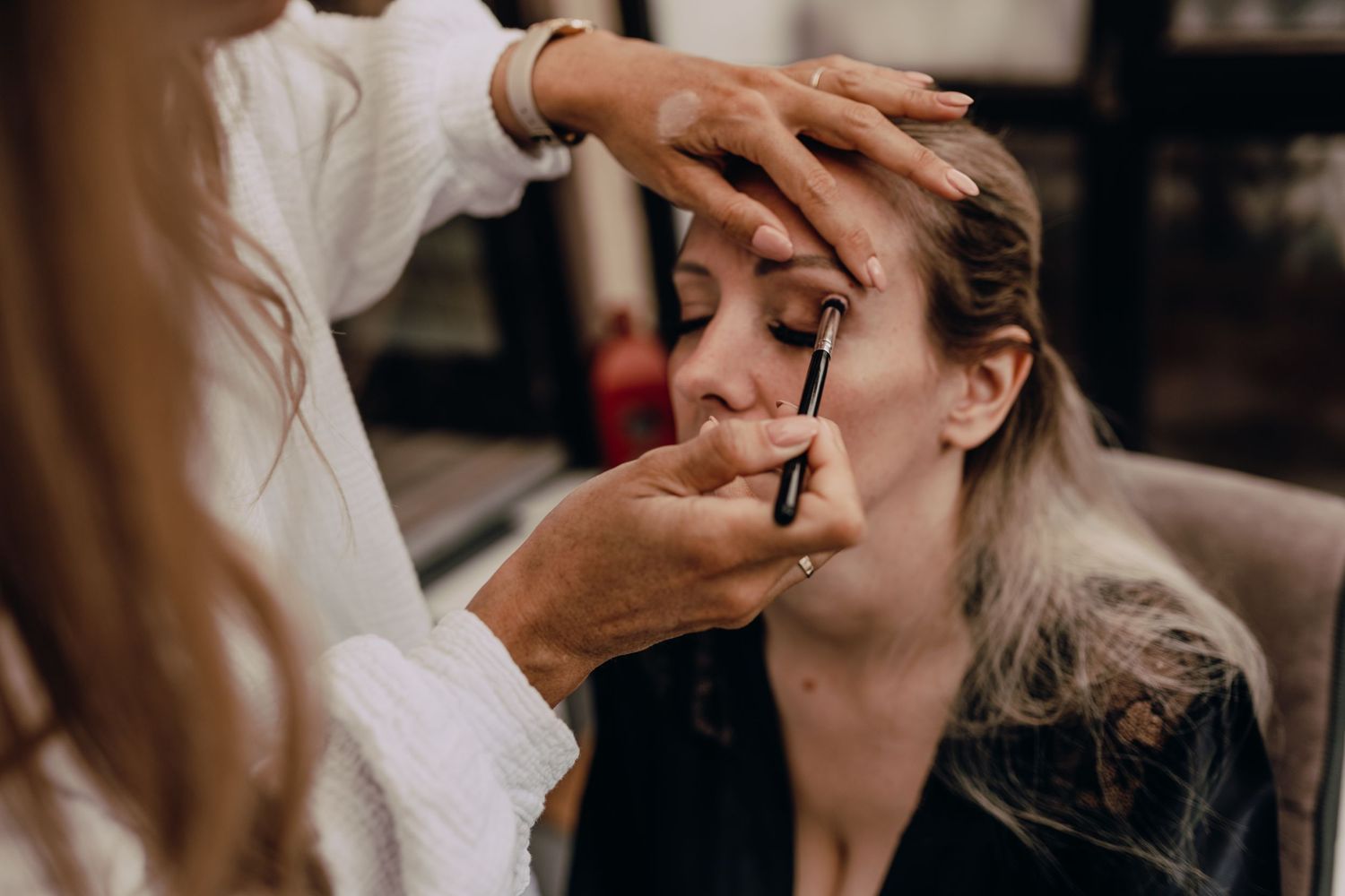 Makeup artist applies cosmetics to a client's face during a professional beauty session in warm lighting.
