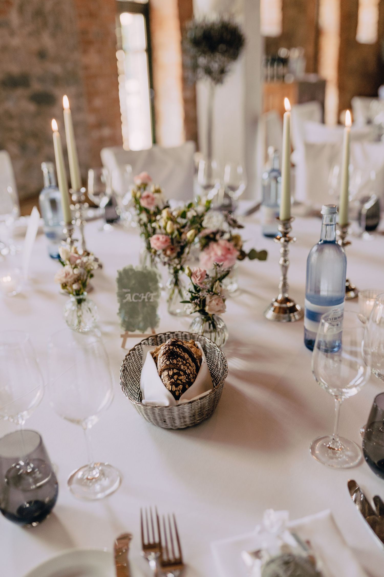 Elegant wedding table setting with candles, flowers and wine glasses on white tablecloth.