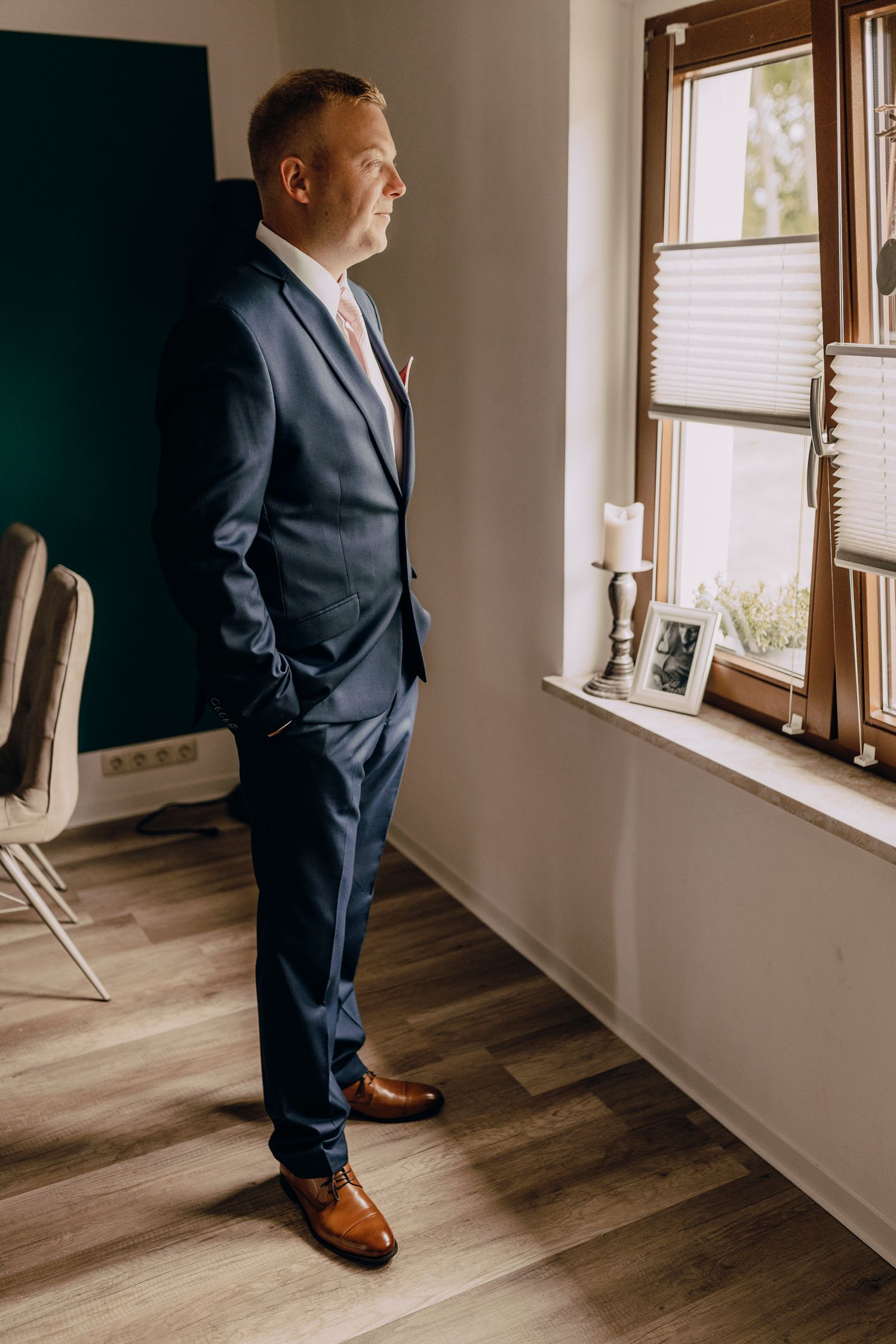 Four angles of a person in a navy suit and brown shoes standing by a window in a room with hardwood floors.