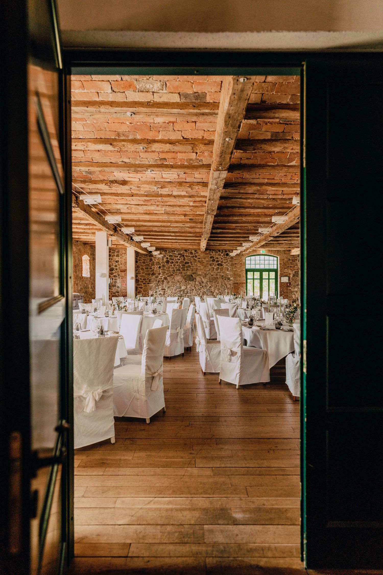 Elegant reception hall with exposed brick walls and white-covered chairs set for wedding celebration.