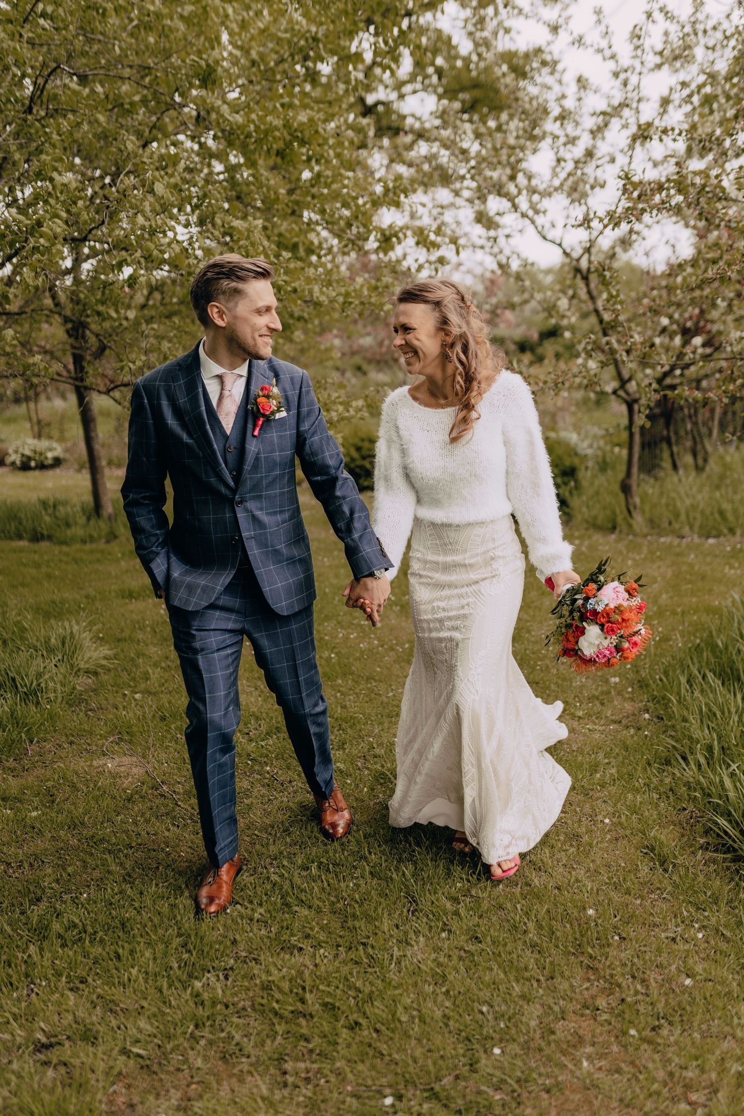 A couple walks hand in hand through an autumn orchard on their wedding day.