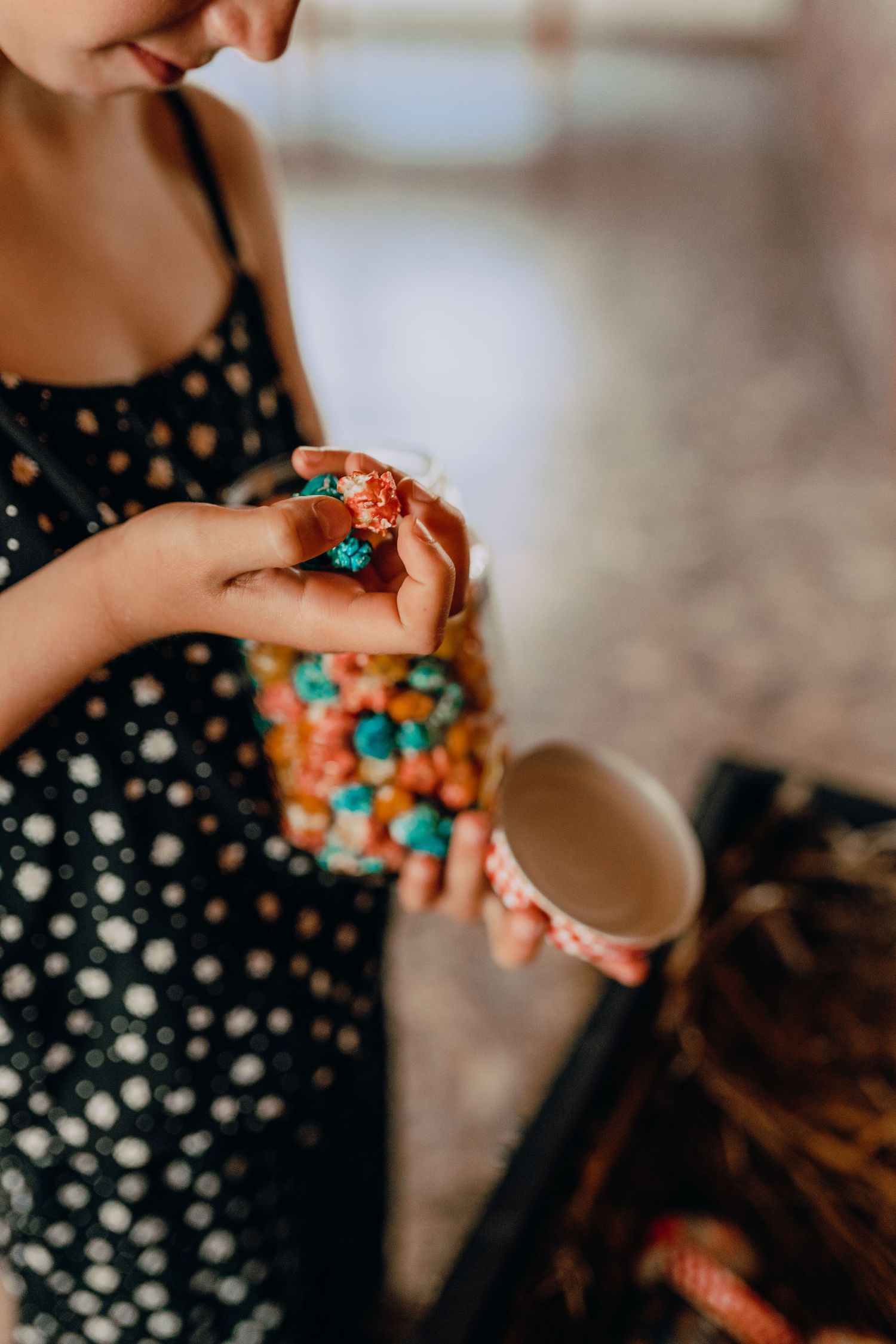 Hands hold colorful candies in a polka dot dress against a light background.