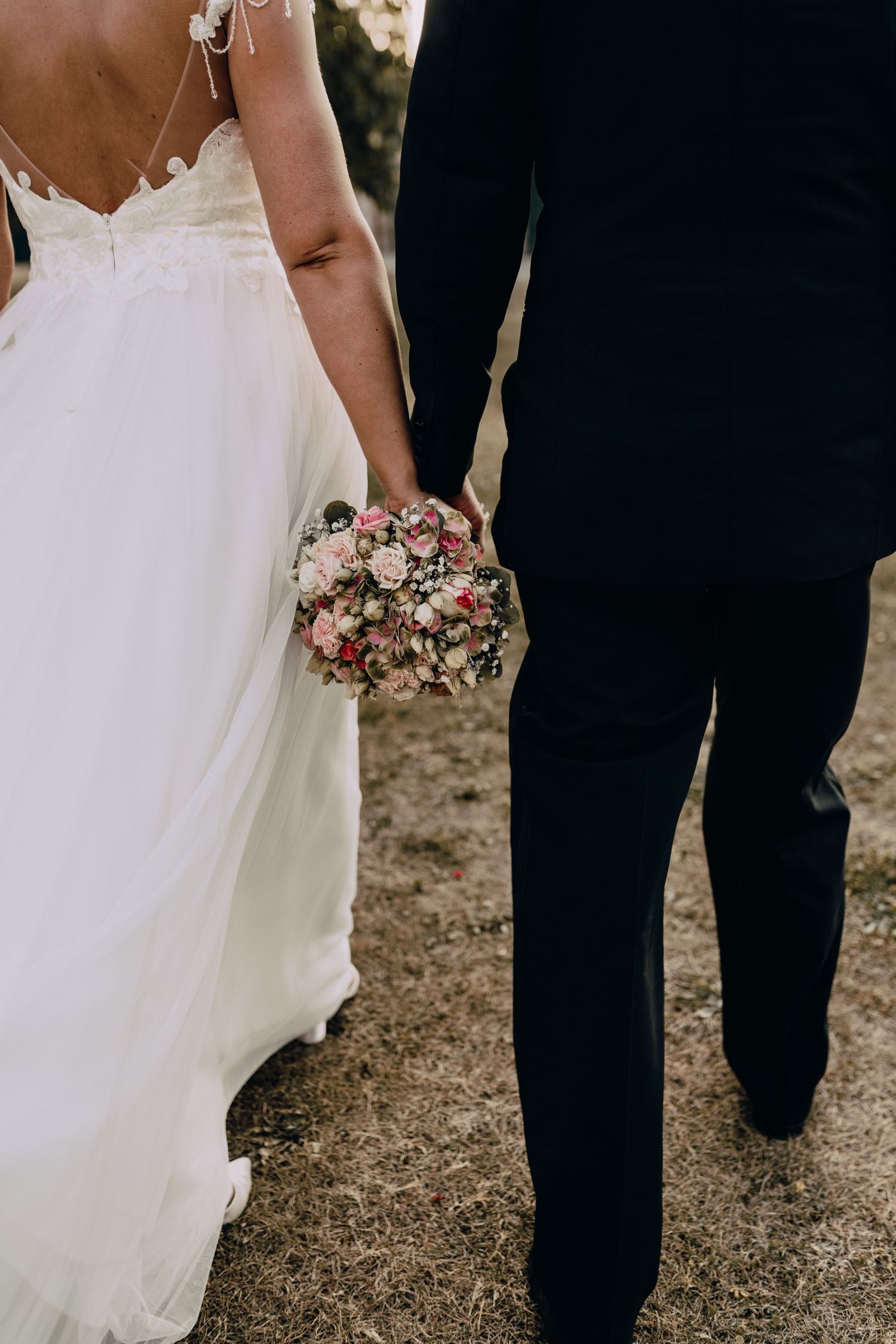 Close-up of white wedding dress and black formal wear as couple stands together outdoors.