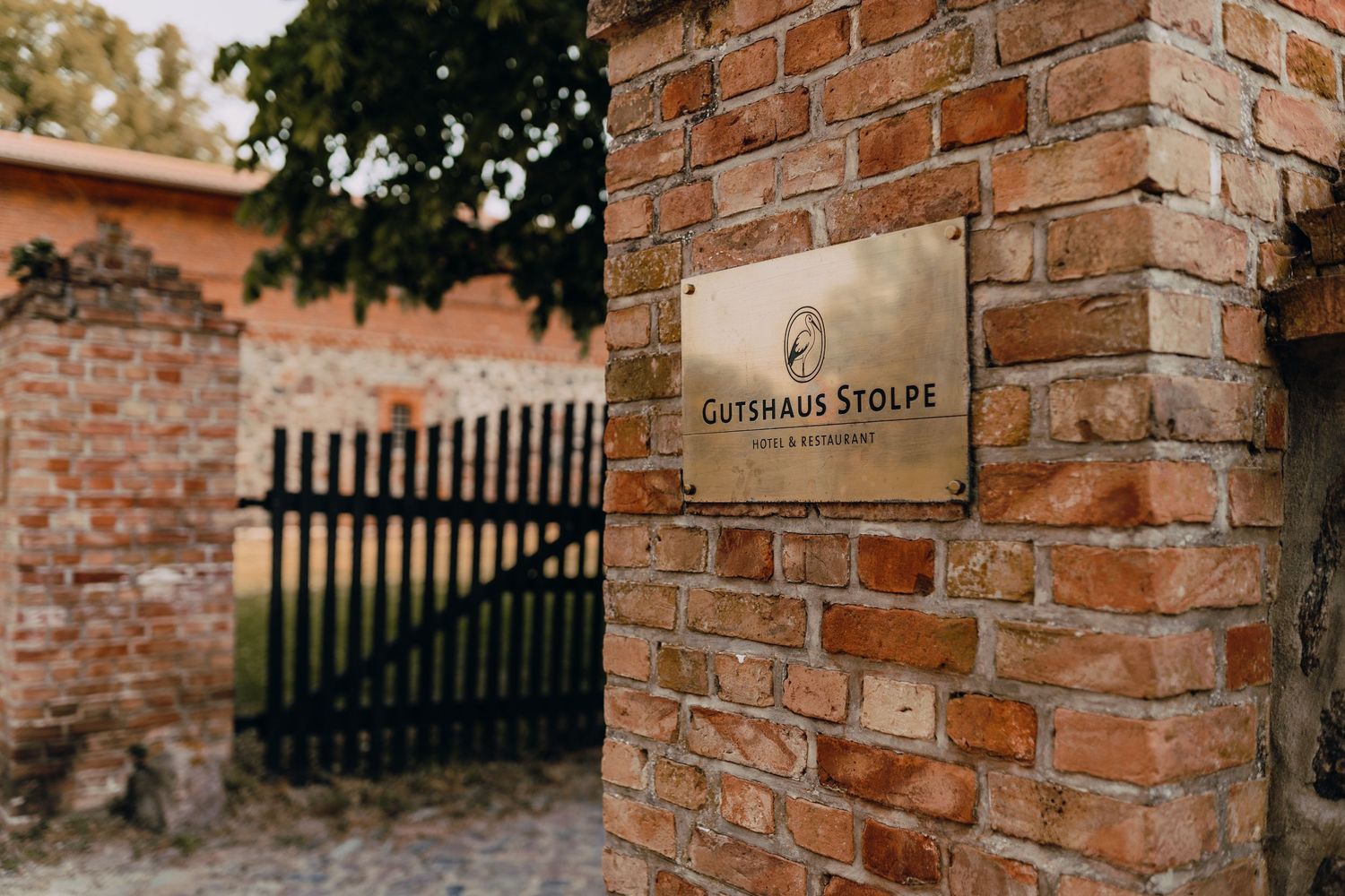 Rustic brick entrance with a metal nameplate mounted on the wall and iron gate in the background.