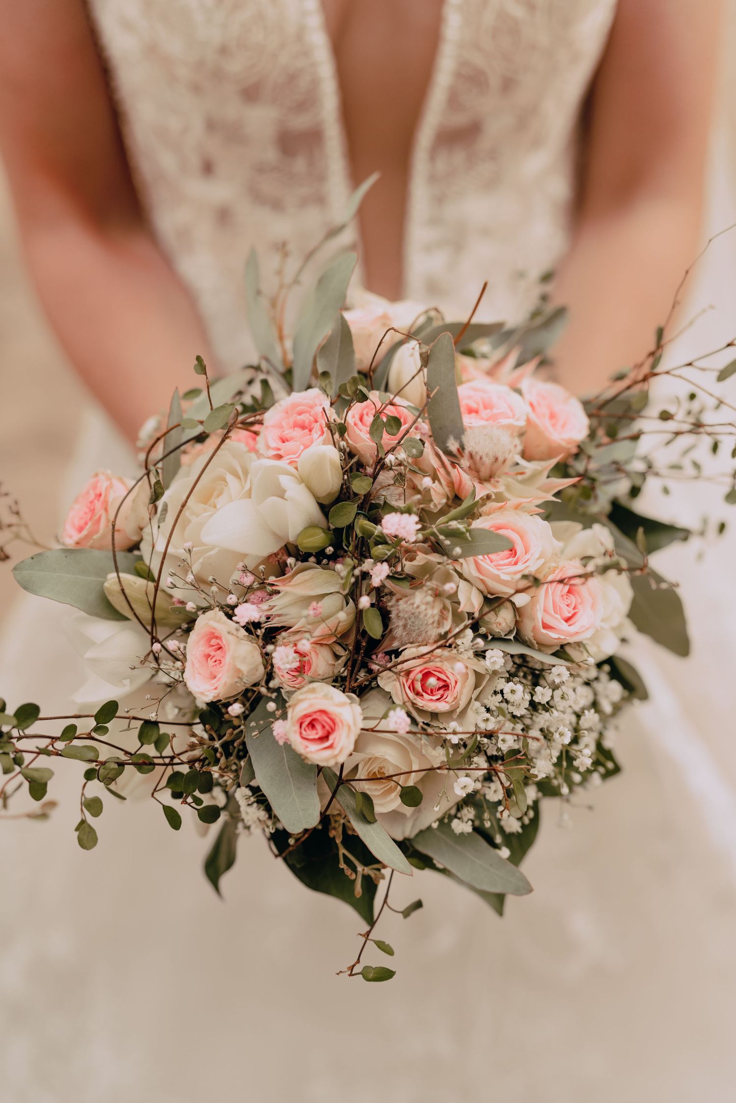 A romantic bridal bouquet featuring pink roses, white baby's breath and eucalyptus leaves held against a white dress.