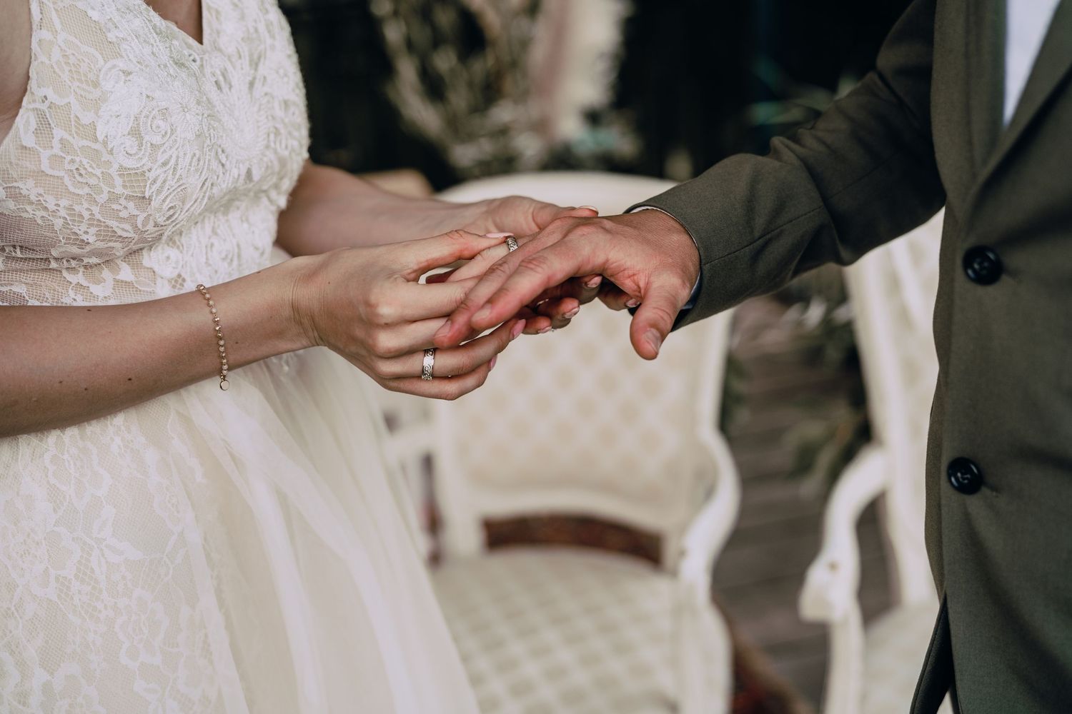 Close-up of hands exchanging wedding rings during an outdoor ceremony.