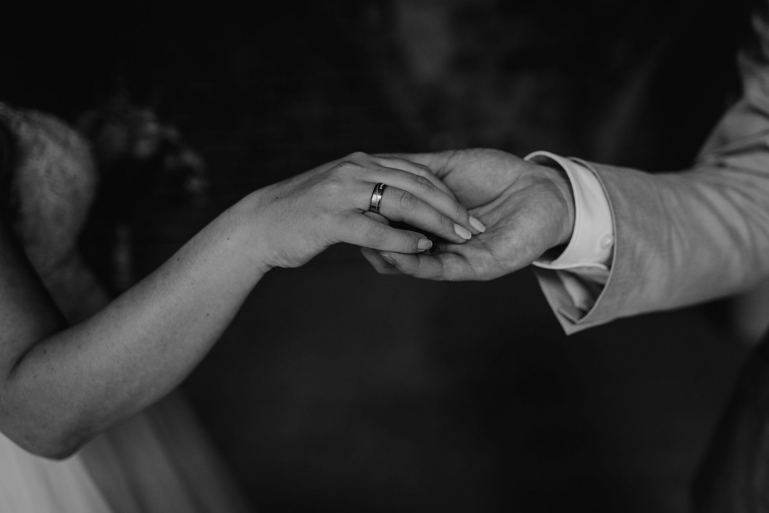 Black and white close-up of hands with wedding rings in an intimate moment.