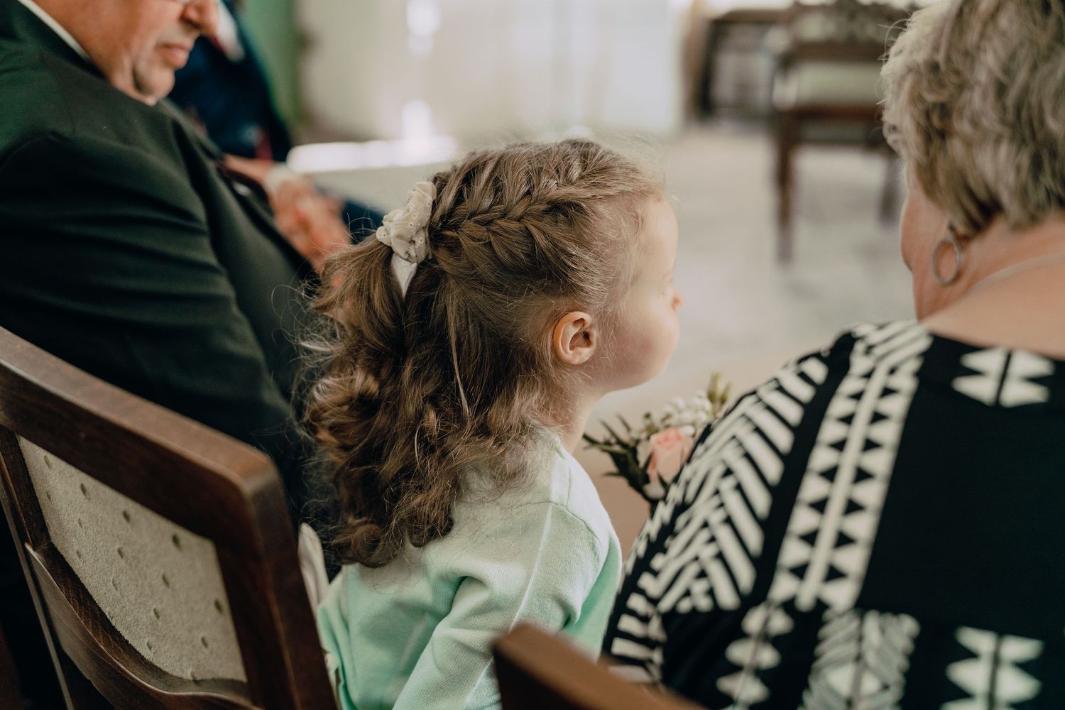 A young child with curled hair watches from behind during a formal event.