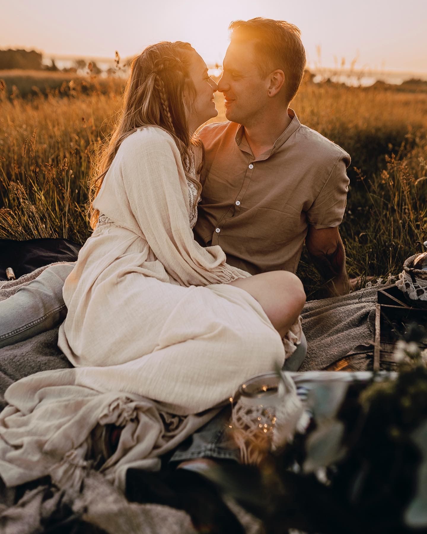 A romantic couple shares an intimate moment at sunset in a golden field while sitting on a blanket.