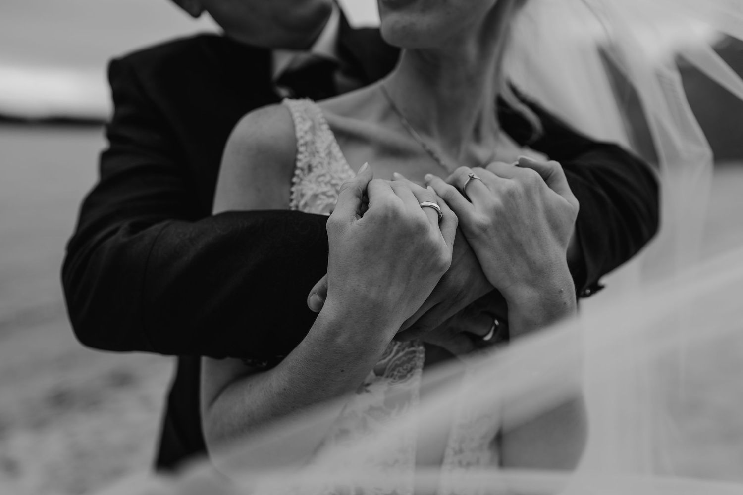 A romantic black and white close-up of a couple's hands clasped together with a wedding veil in the background.
