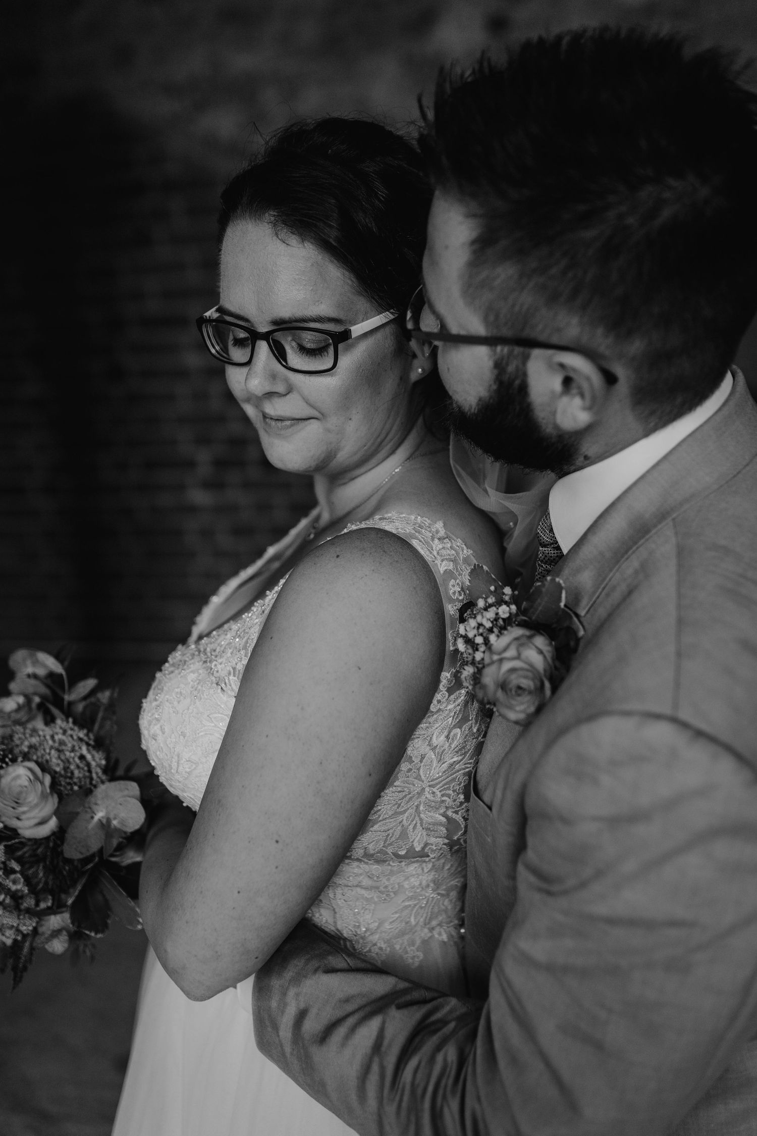 Black and white portrait of newlyweds in an intimate pose against brick wall backdrop.