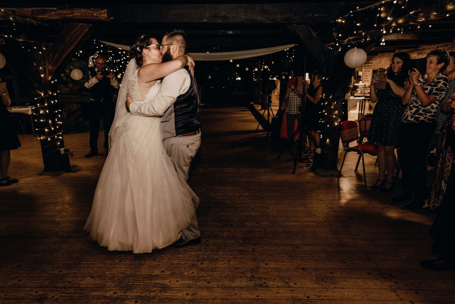 Newlyweds dancing in a cozy venue illuminated by warm string lights and candles.