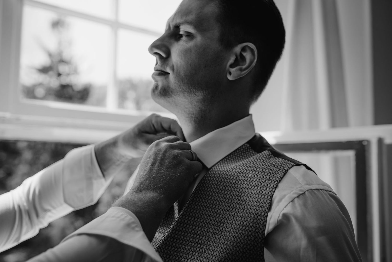A black and white image showing hands adjusting a tie on someone wearing a formal vest and dress shirt.
