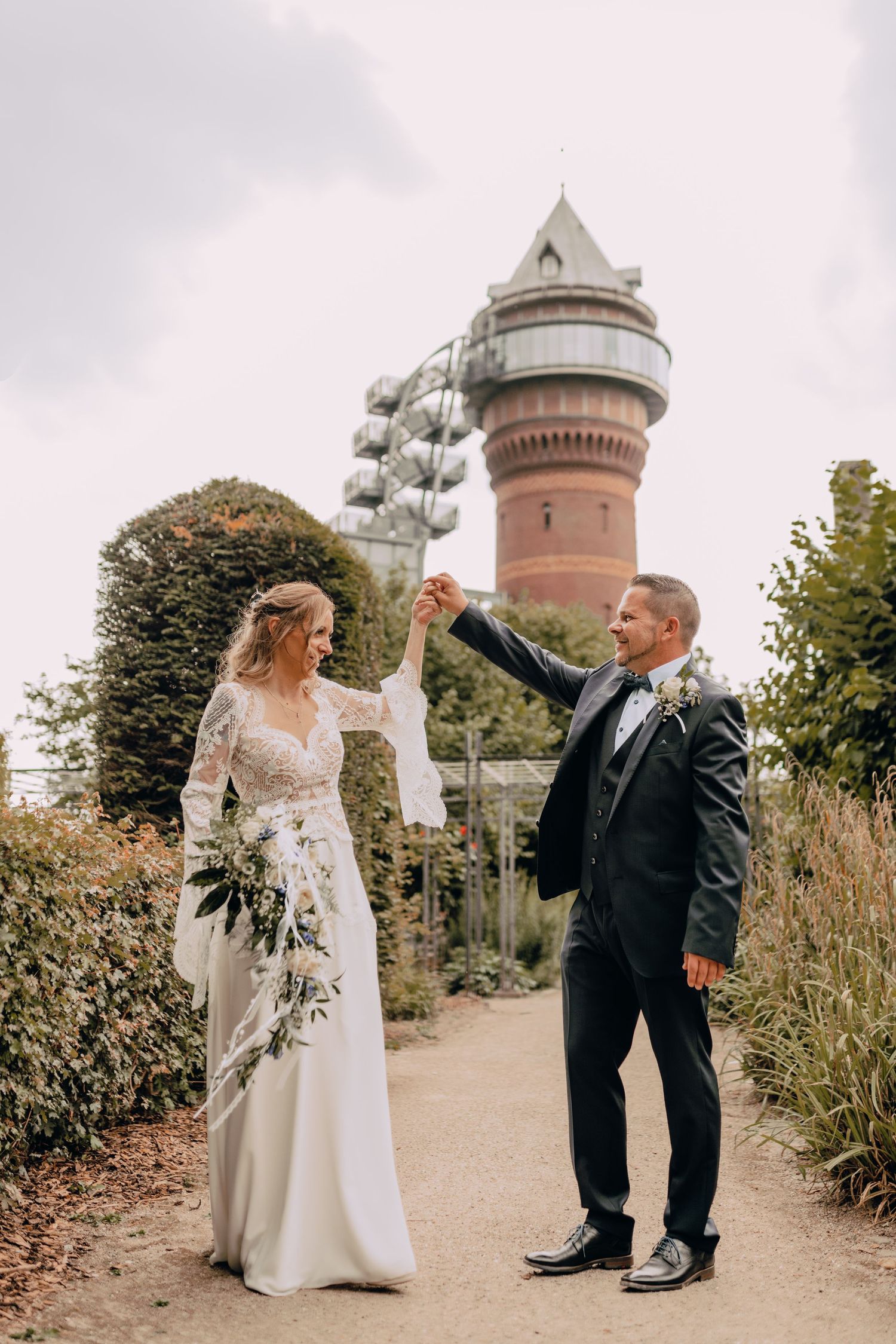 A wedding couple dances together in front of a historic brick water tower on an autumn day.