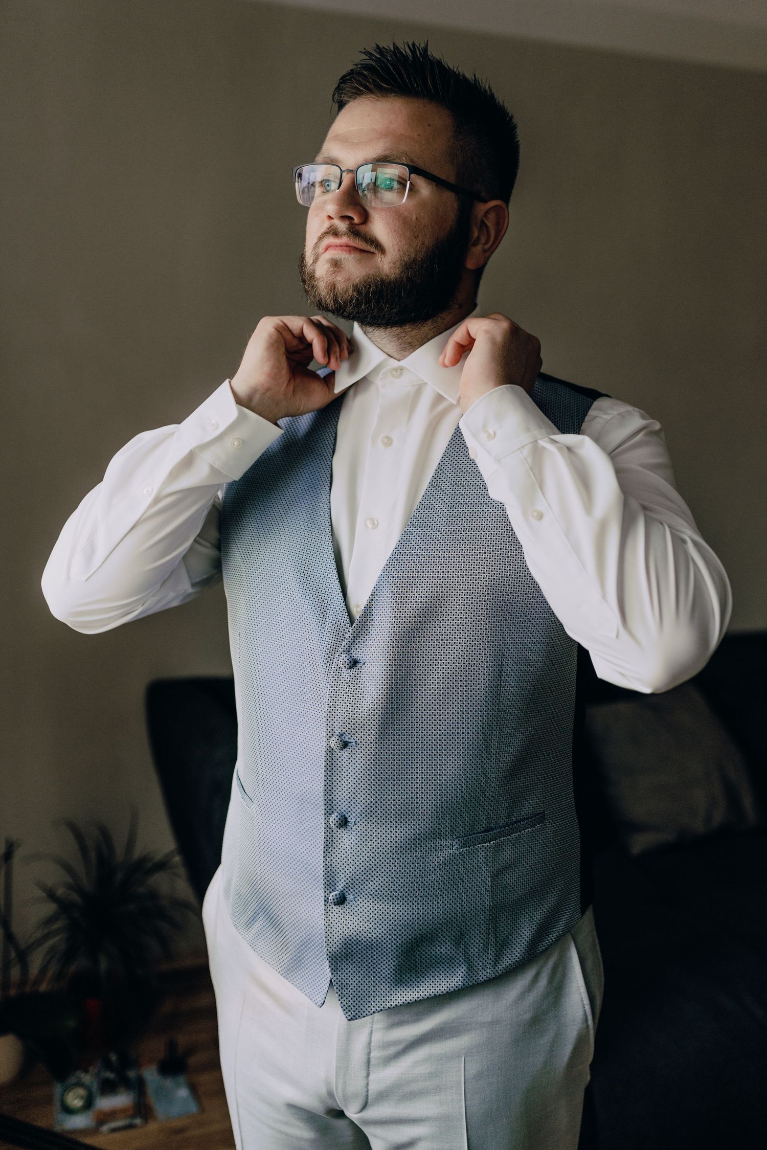 A grey vest with white dress shirt being adjusted in an indoor setting.