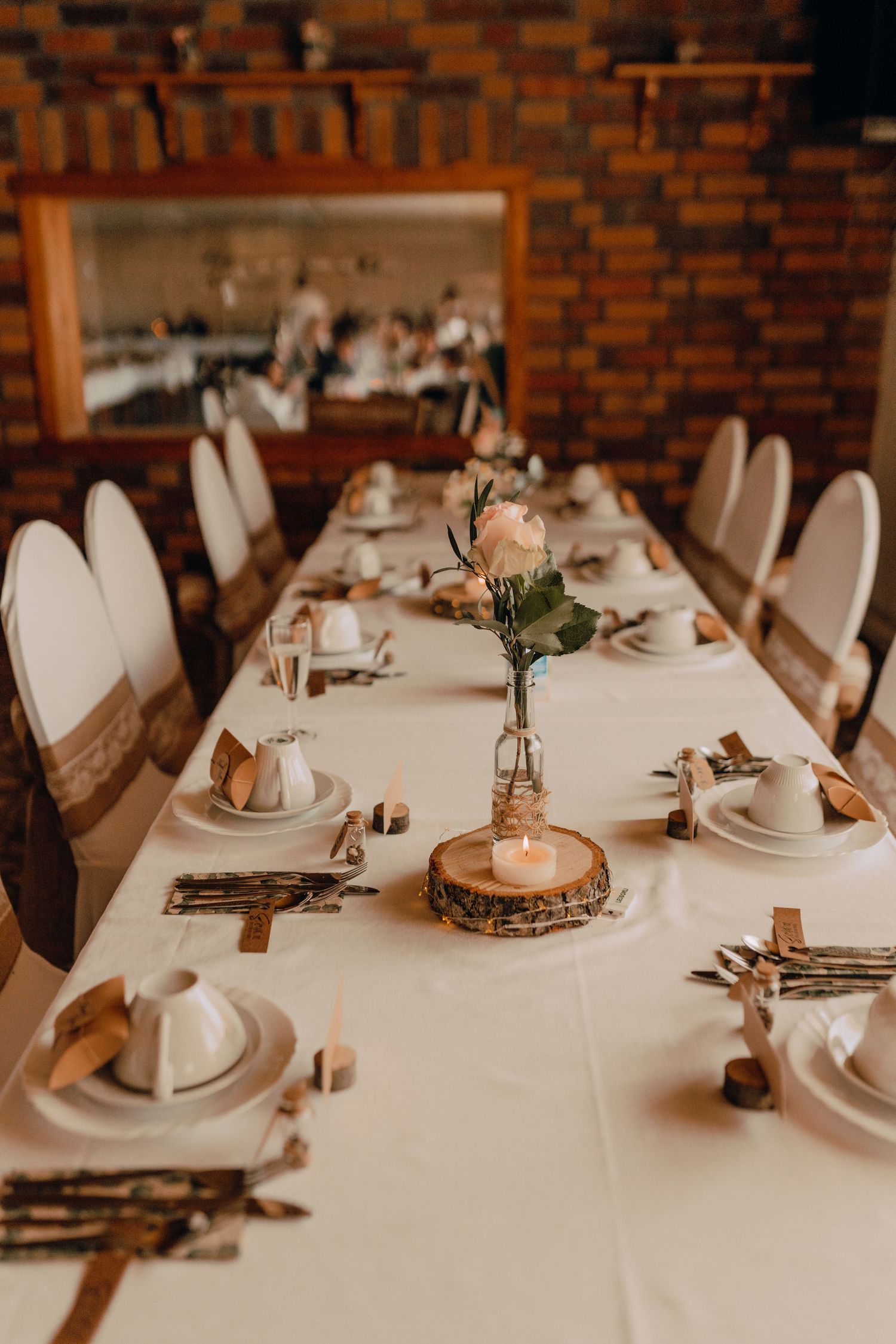 Rustic wedding reception table with white linens and wooden decor features elegant place settings and delicate floral centerpieces.