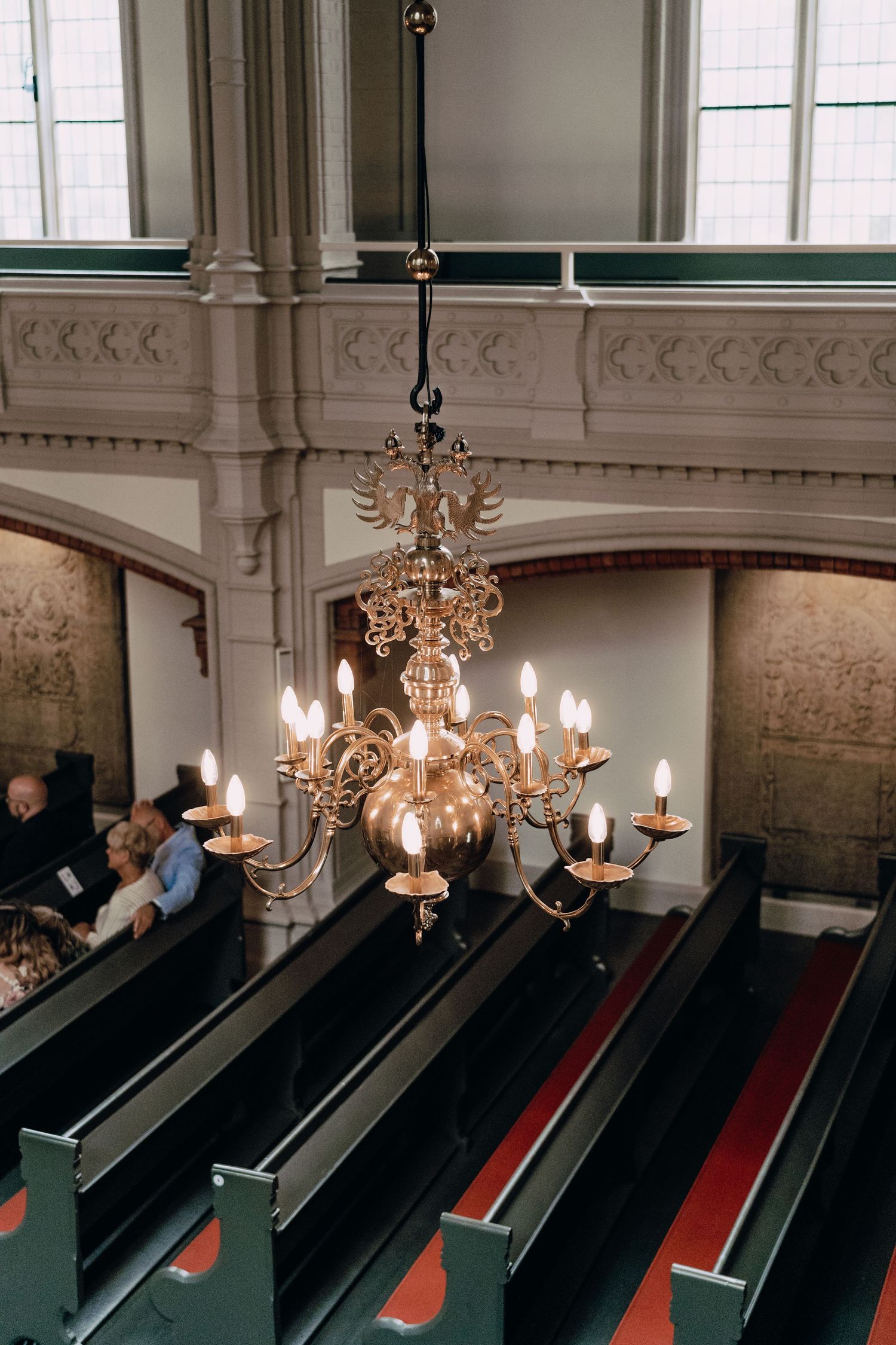 An ornate golden chandelier hangs above wooden church pews in a traditional sanctuary interior.