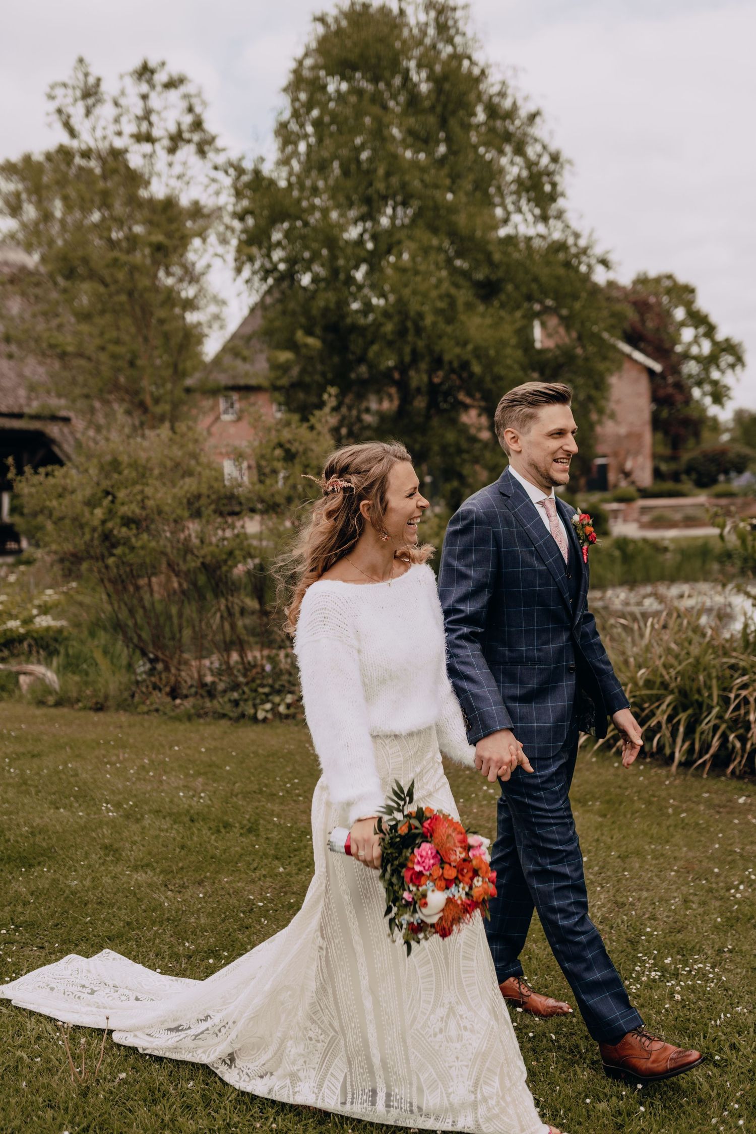 Wedding couple walks together on garden grounds wearing elegant white dress and navy checkered suit.